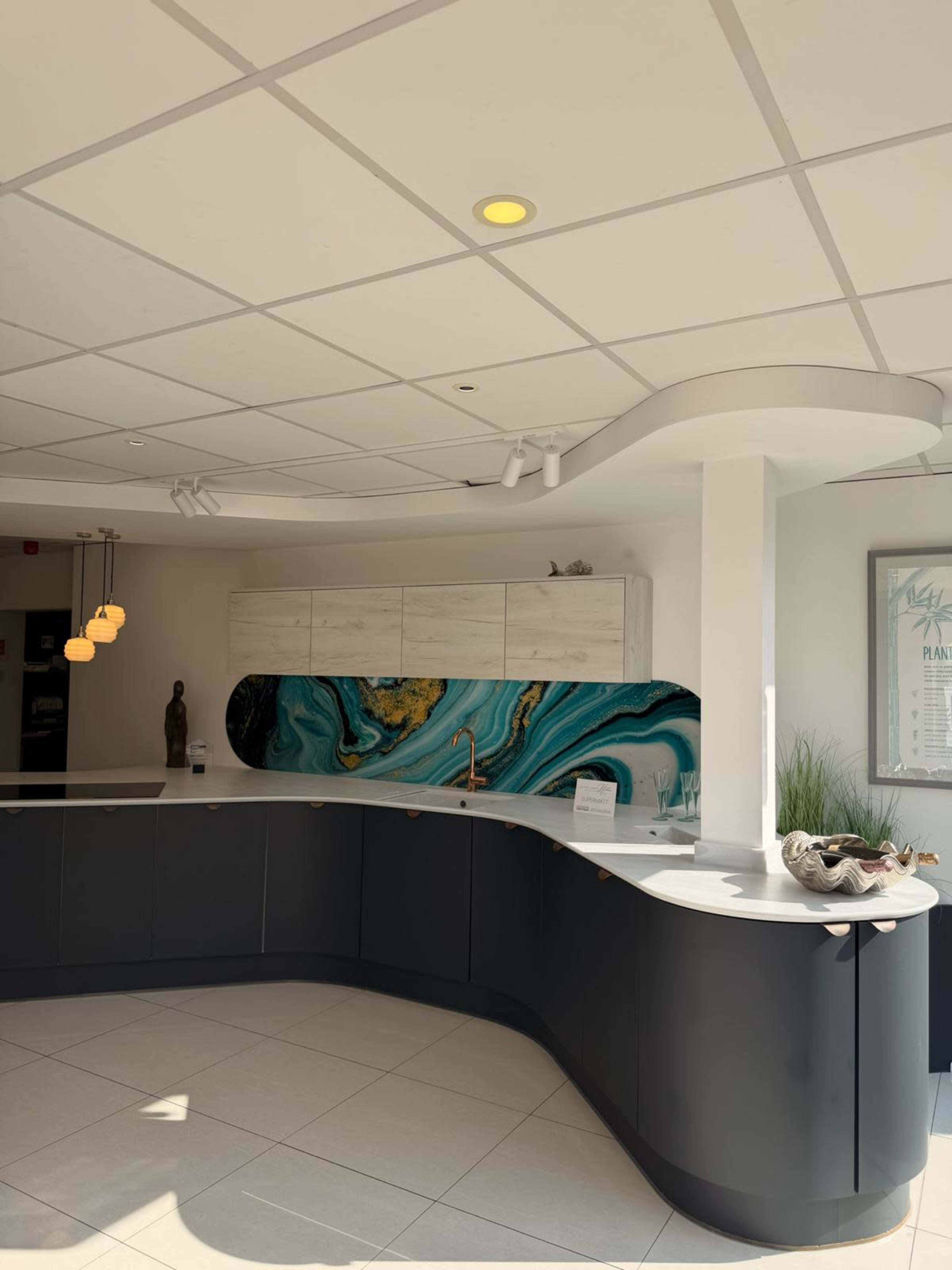 The image shows a modern kitchen with a curved black counter and a blue-green marbled backsplash, complemented by sleek cabinetry and minimal decor.
