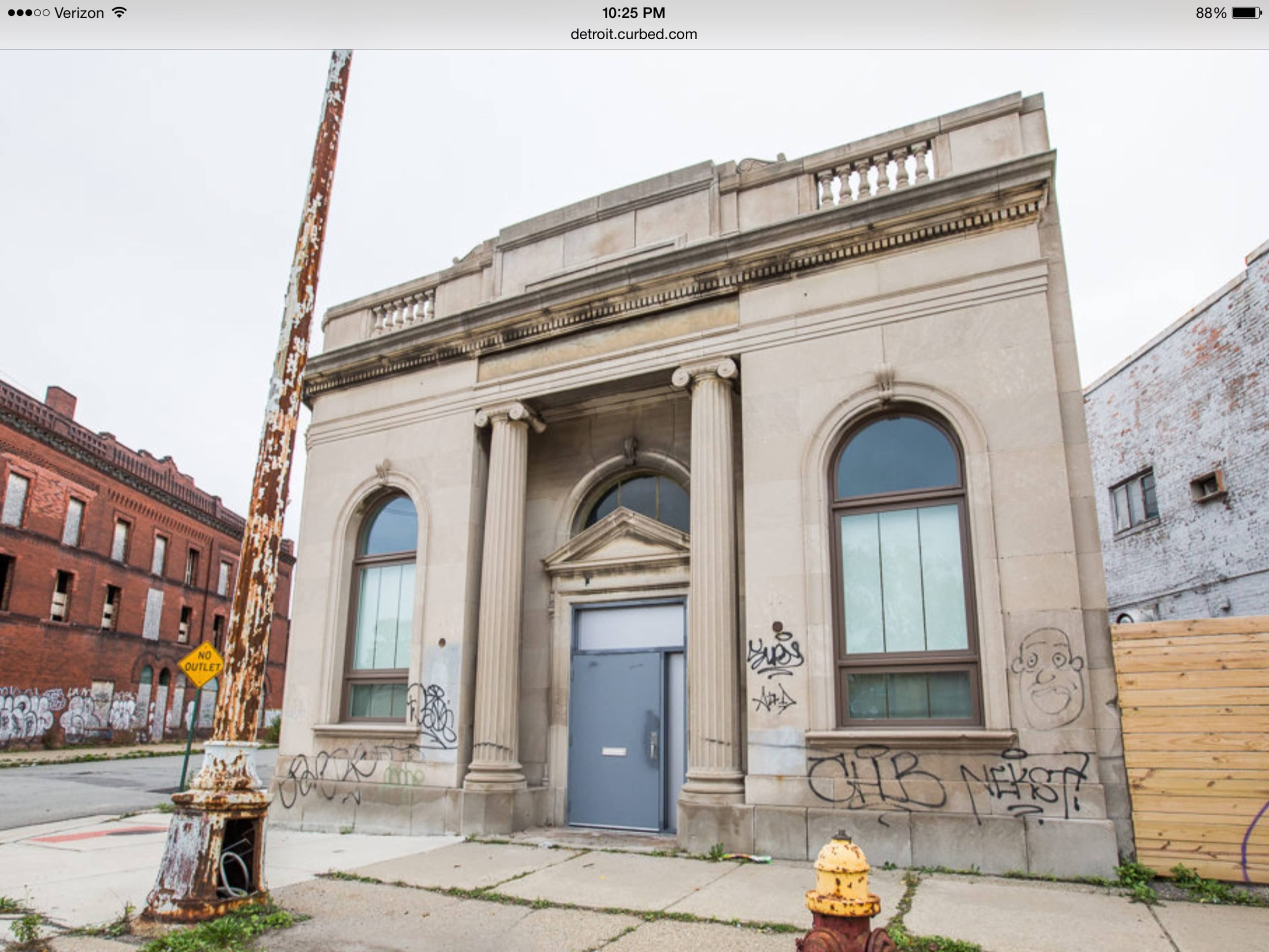 A weathered, abandoned building with large arched windows and graffiti on its facade, located on a street with a rusty lamppost nearby.