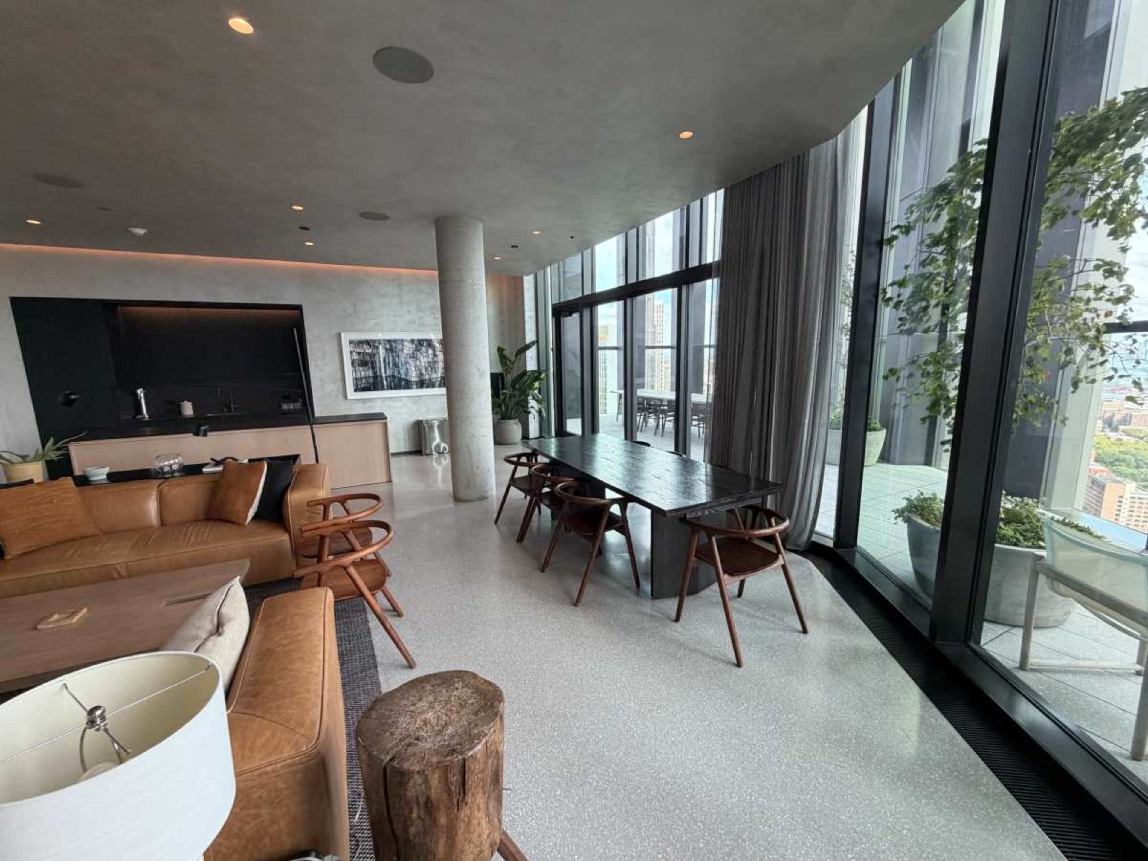 A modern living space features a leather seating area, a dining table, and expansive windows that provide a view of the city skyline.