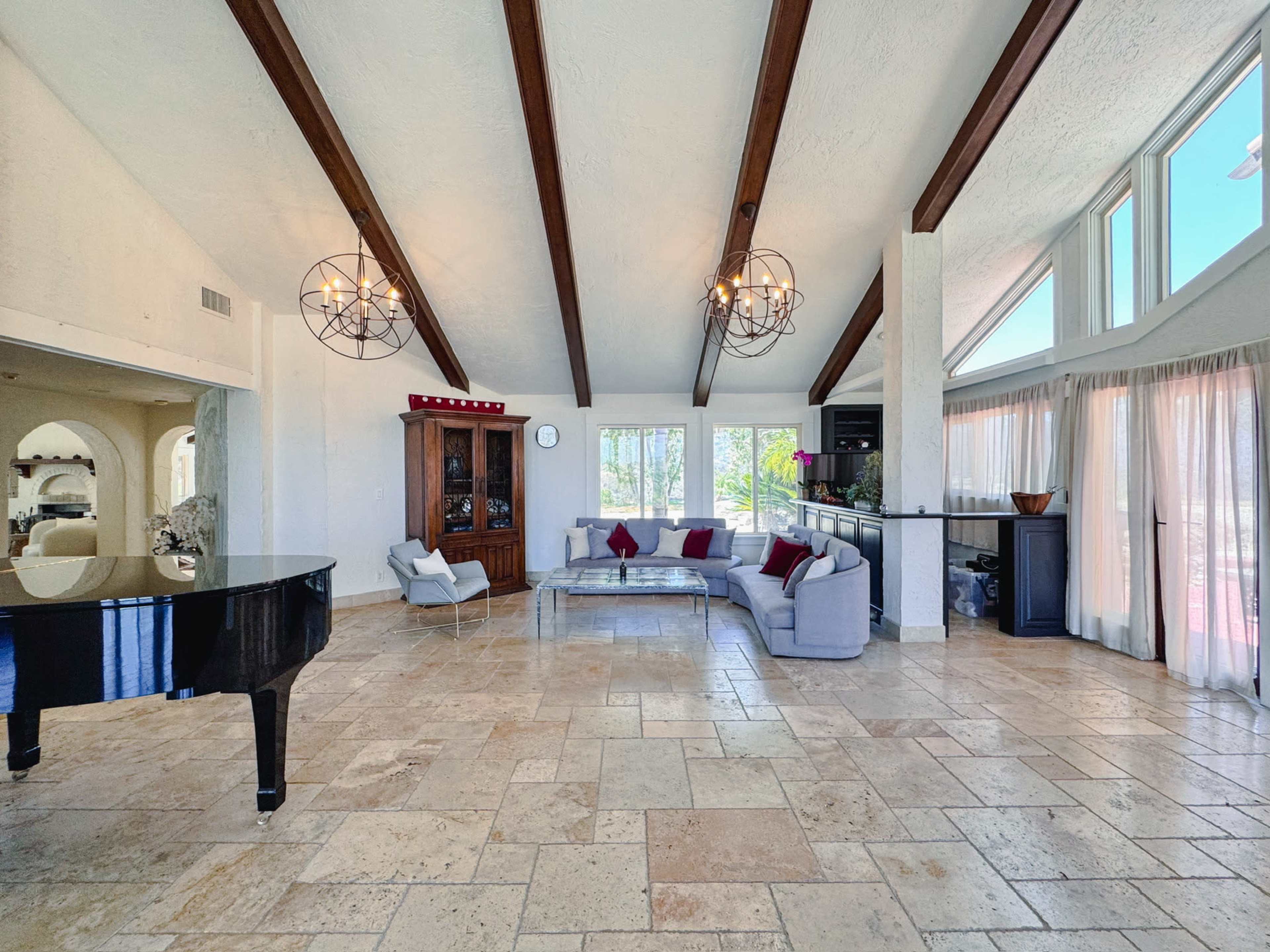 The spacious living room features a grand piano, a sectional sofa, and large windows allowing natural light to fill the space.