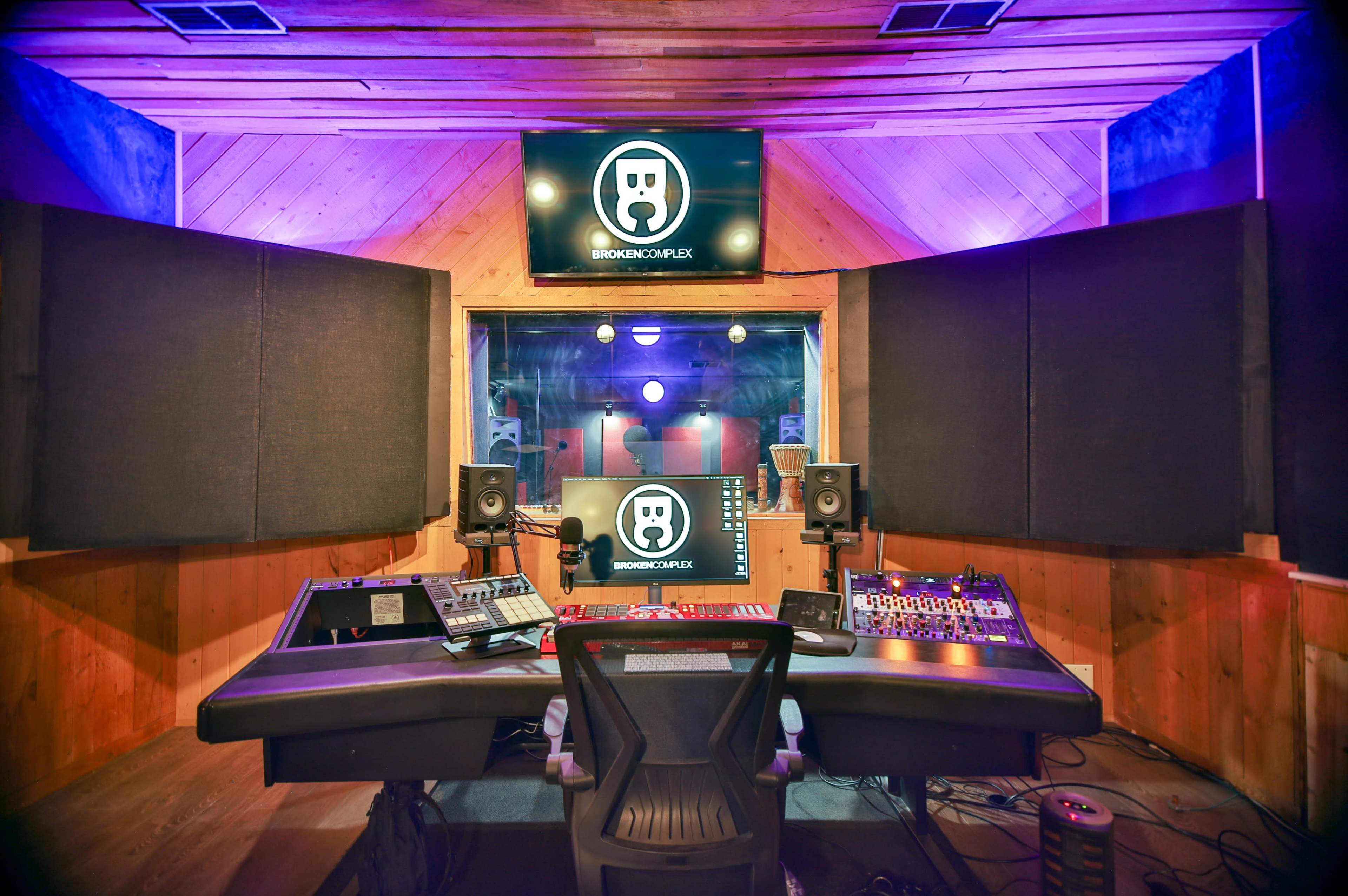 A music production studio featuring a control desk, speakers, and a large screen displaying a logo.