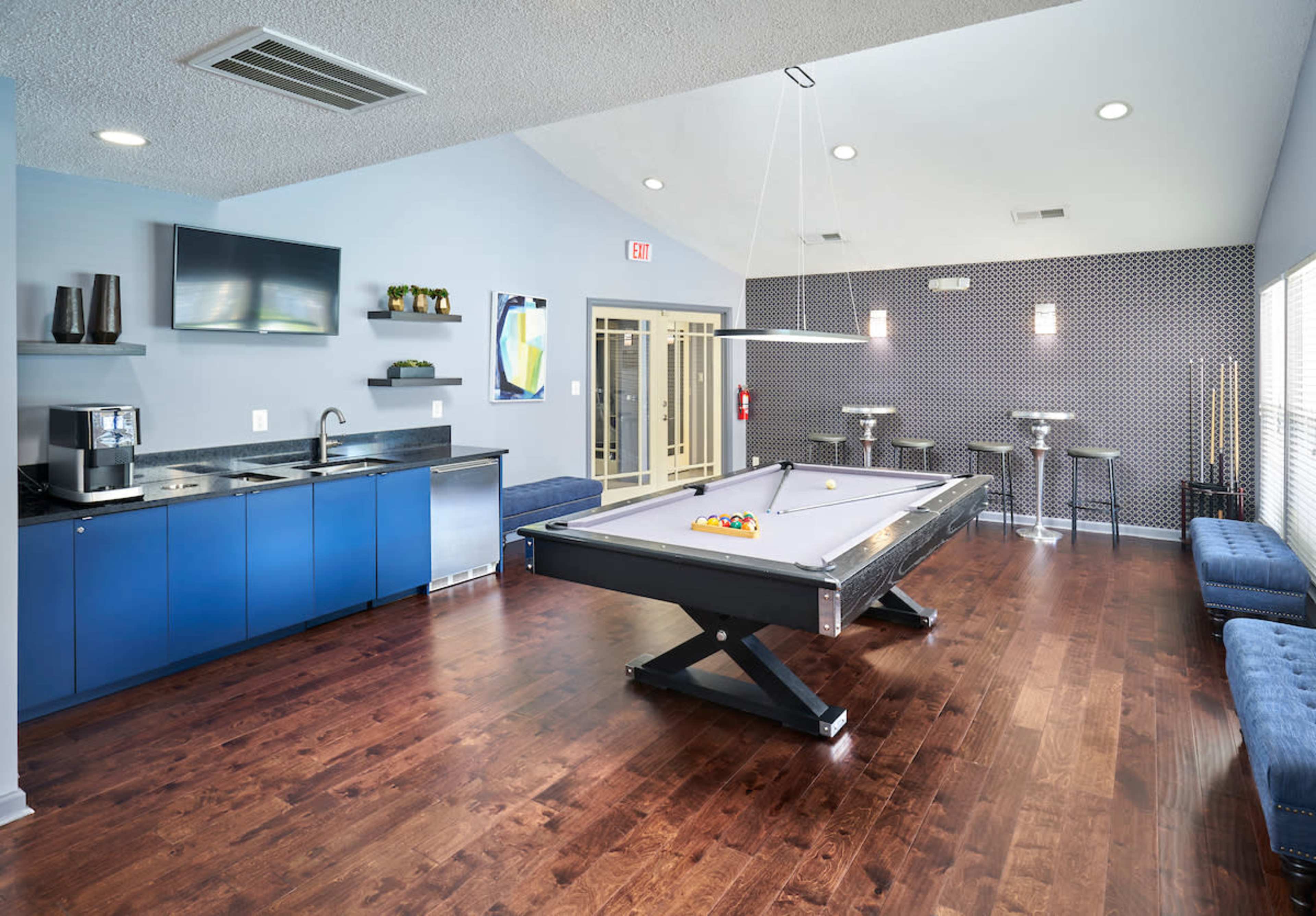 A modern lounge area featuring a pool table, a kitchenette, and seating along the walls.