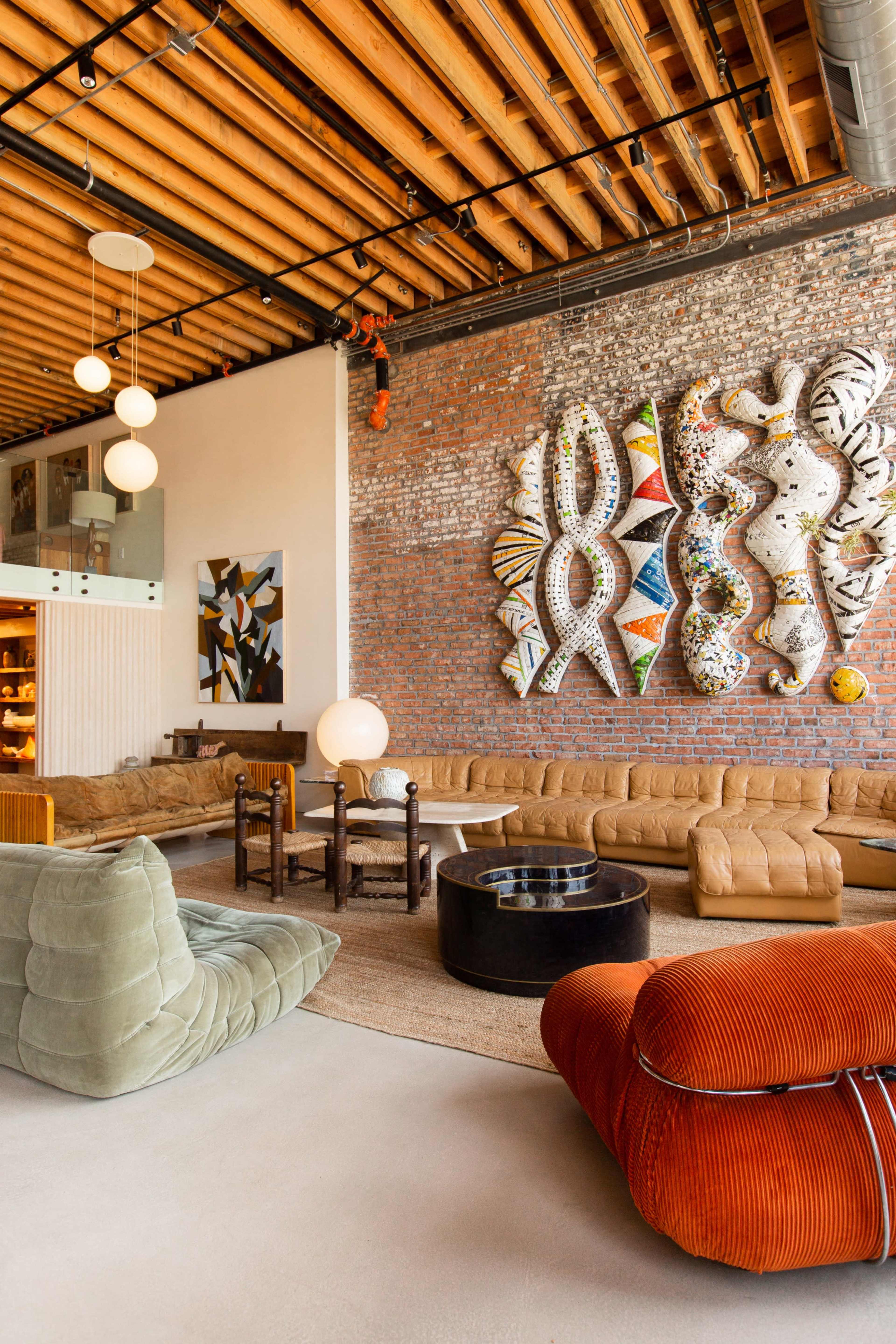 A modern living space featuring a large sectional sofa, a round coffee table, and an artistic wall installation made of colorful materials.