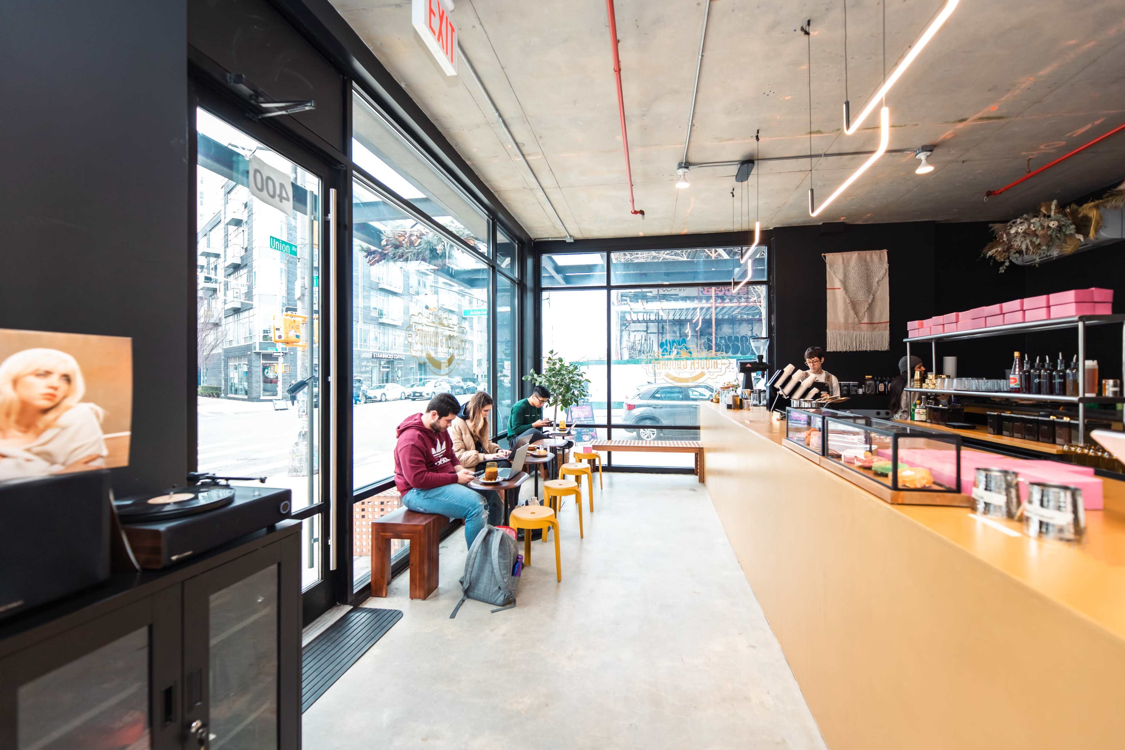 A modern café interior with customers sitting at small tables and a long counter displaying various items.