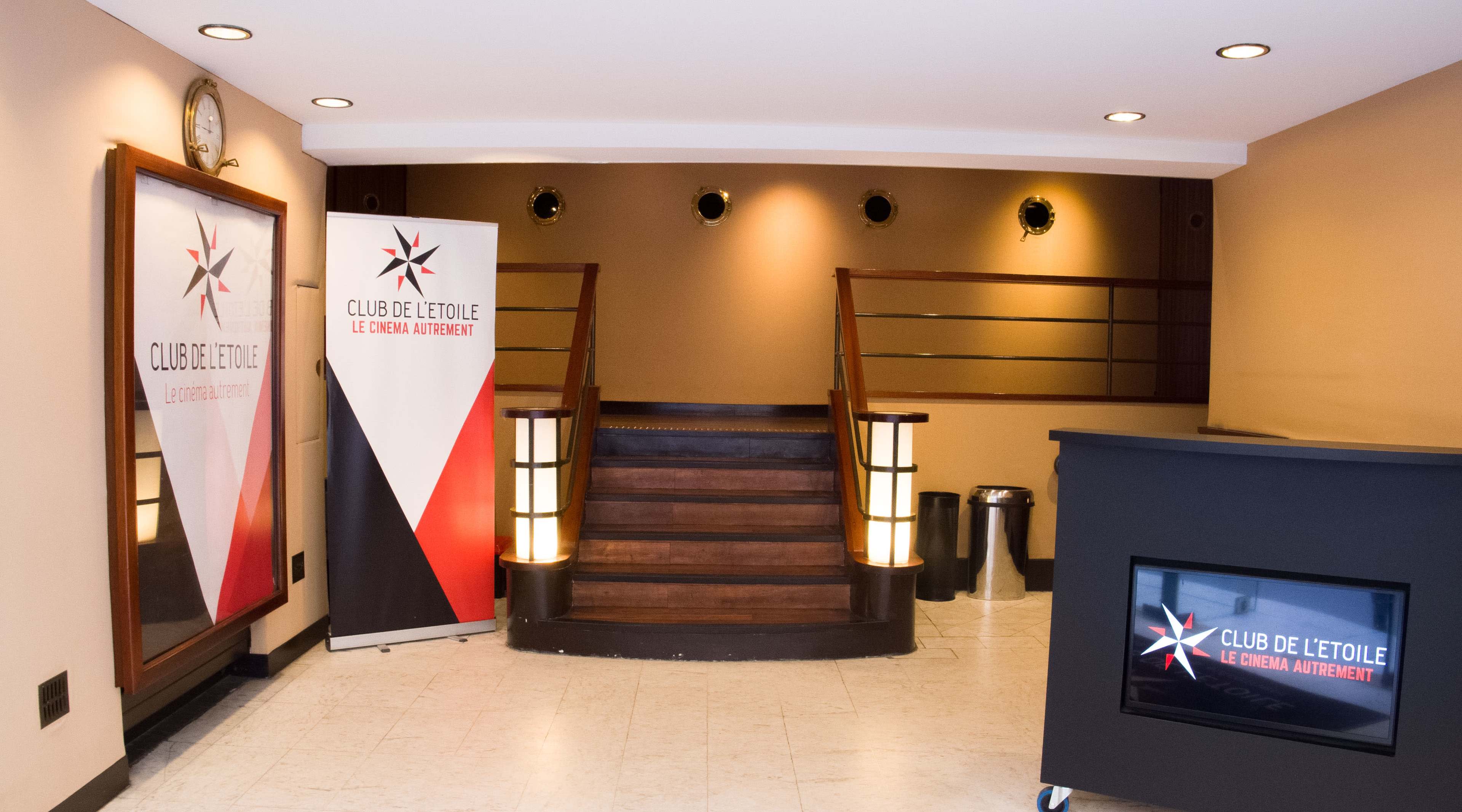 The interior of a venue featuring a reception area with a staircase, banners on either side, and a TV display on a counter.