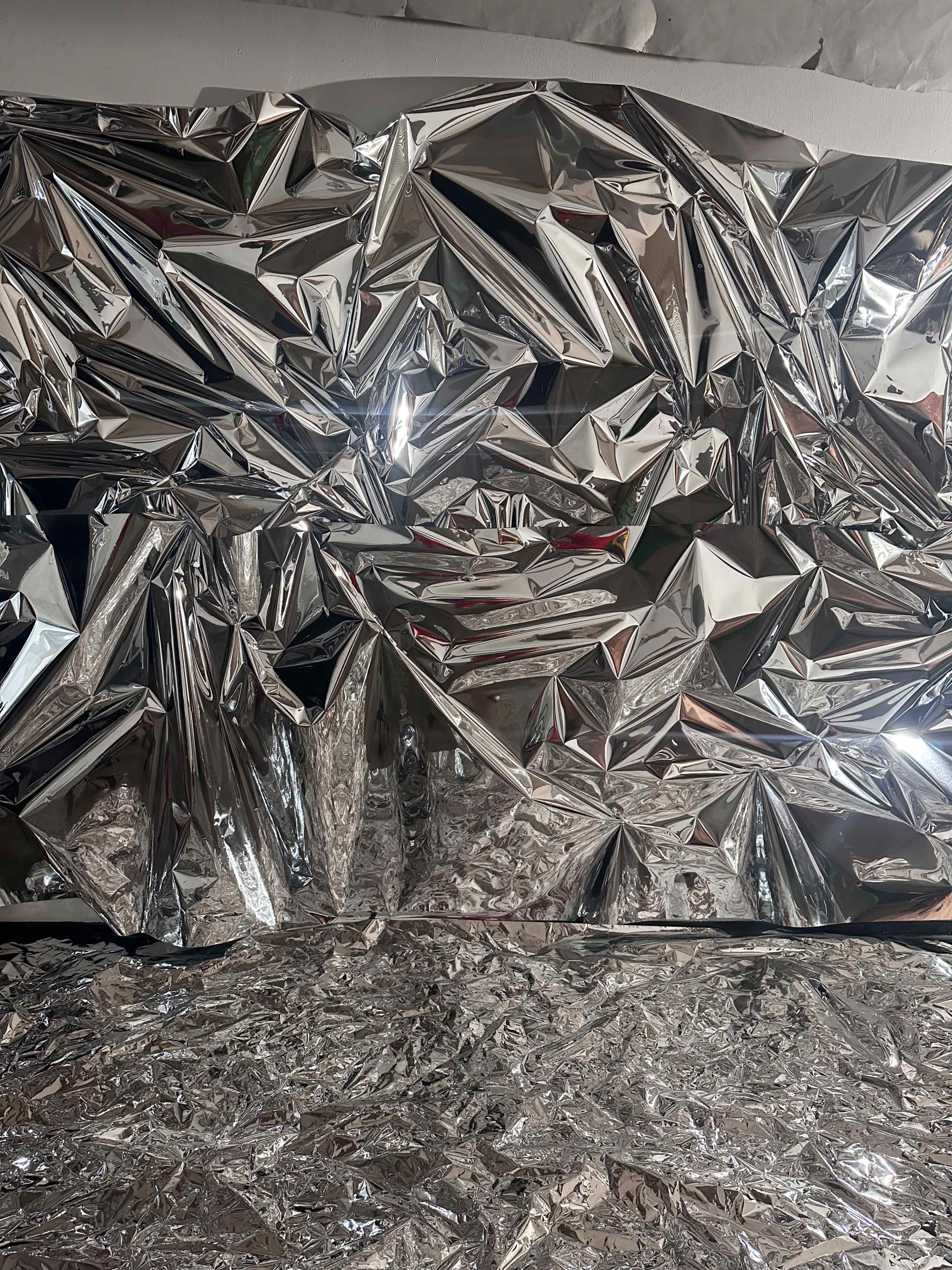 The image shows a crumpled and shiny metallic foil surface, reflecting light and creating a textured appearance.