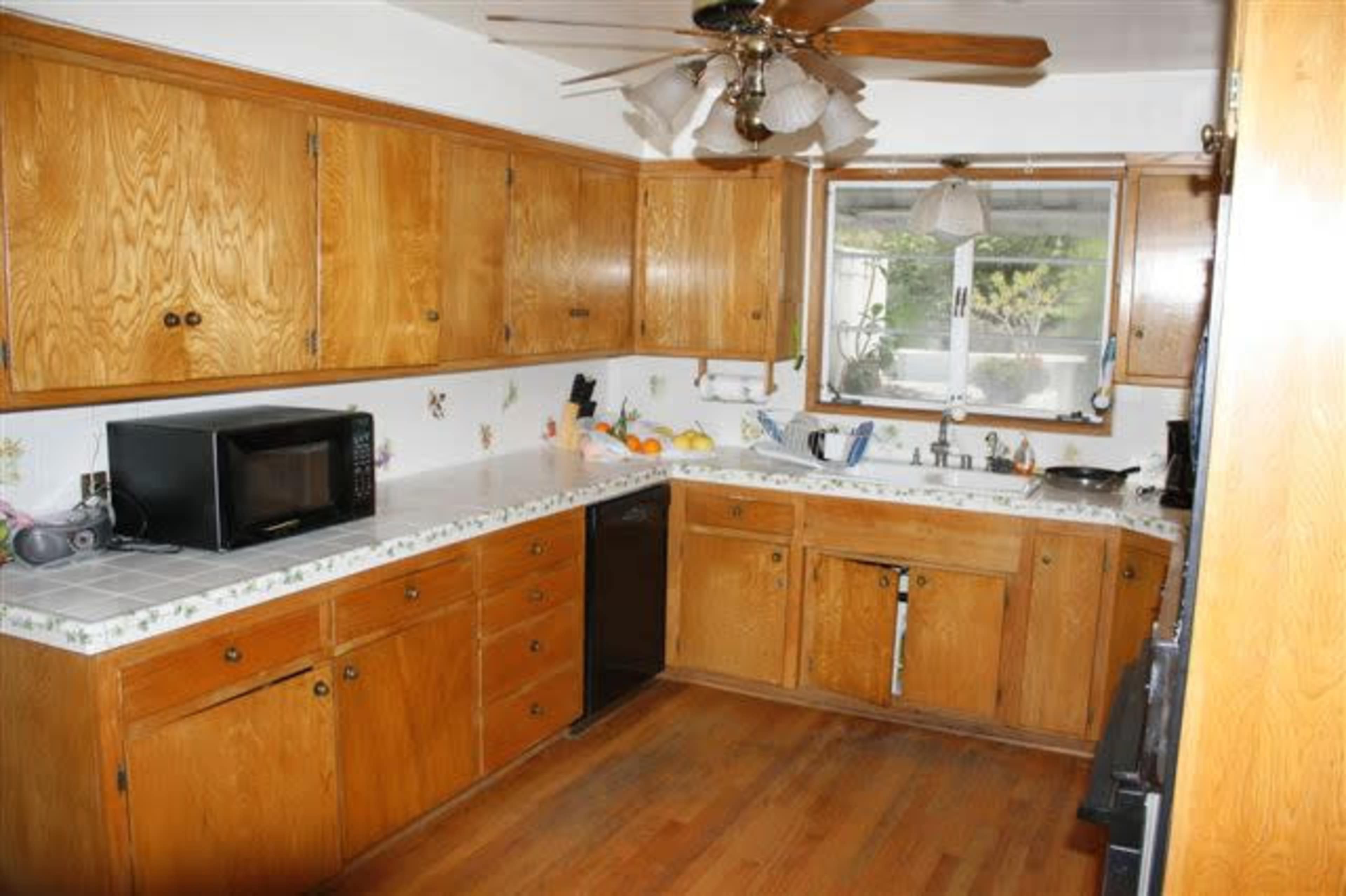 A kitchen features wooden cabinets, a microwave, and a window overlooking a small garden.