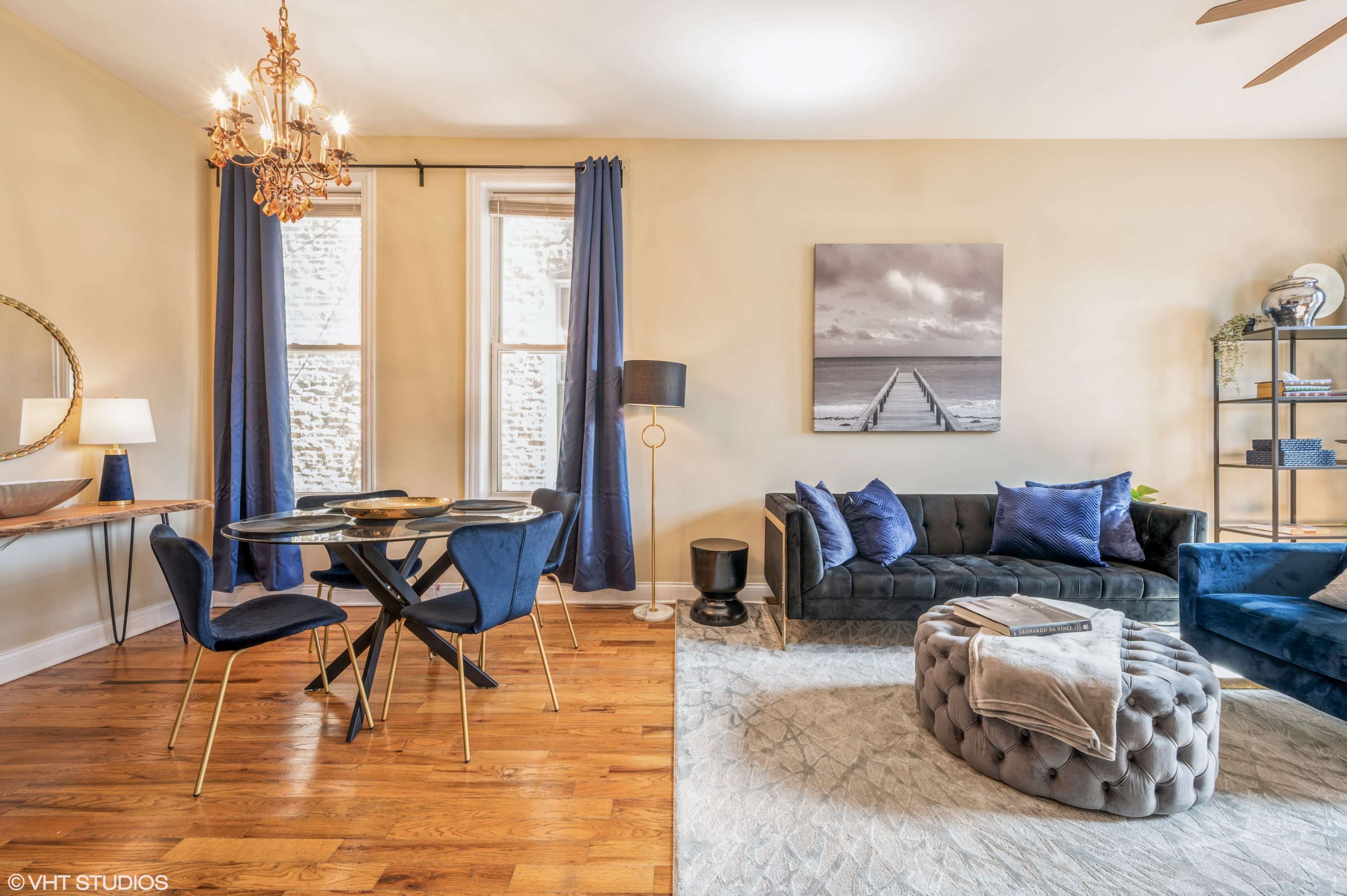 A stylish living area with a black sofa, a round dining table, and decorative elements including a large wall photograph and blue curtains.