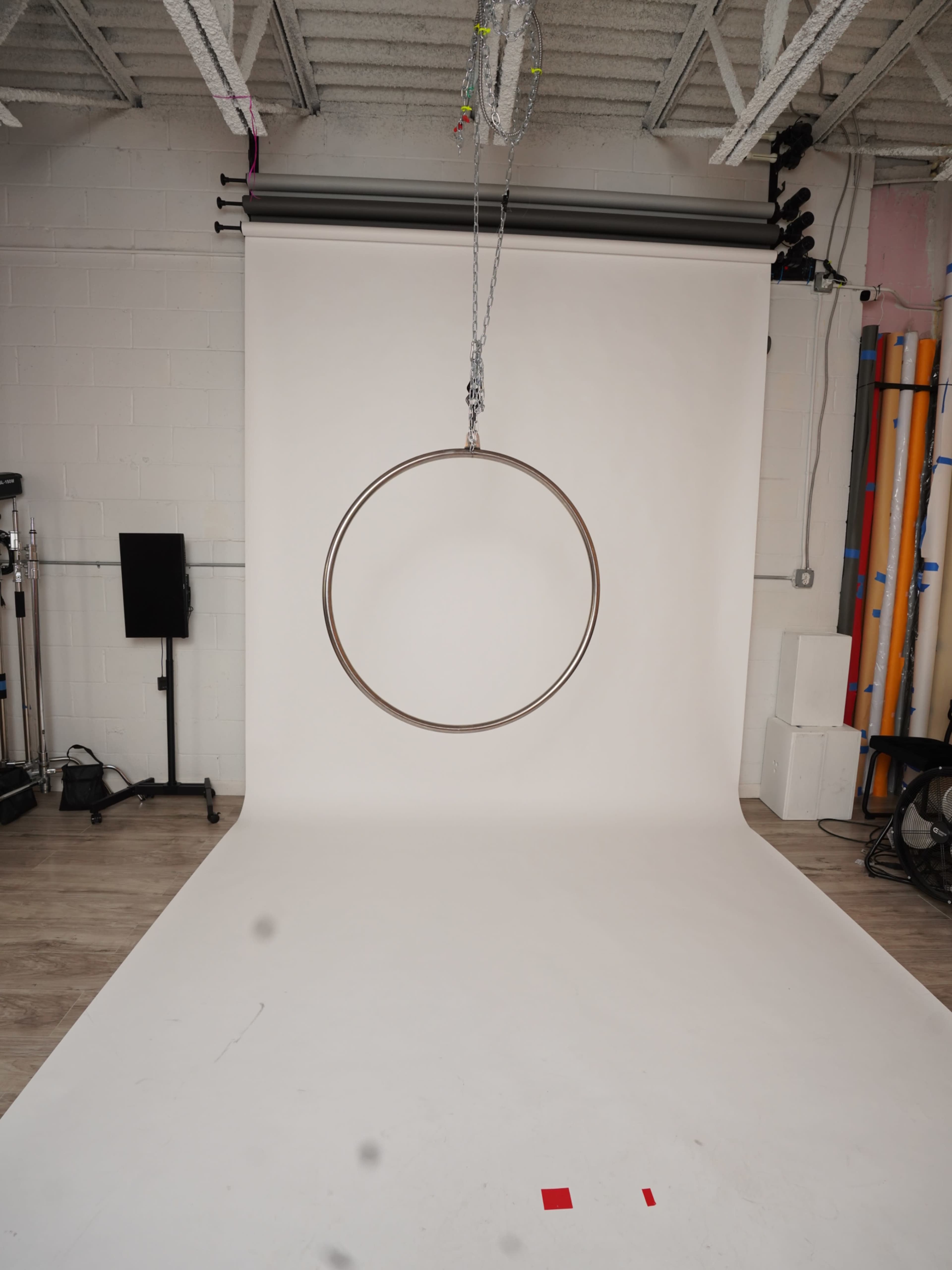 The image shows a large metal hoop suspended from the ceiling in a studio with a plain white backdrop.