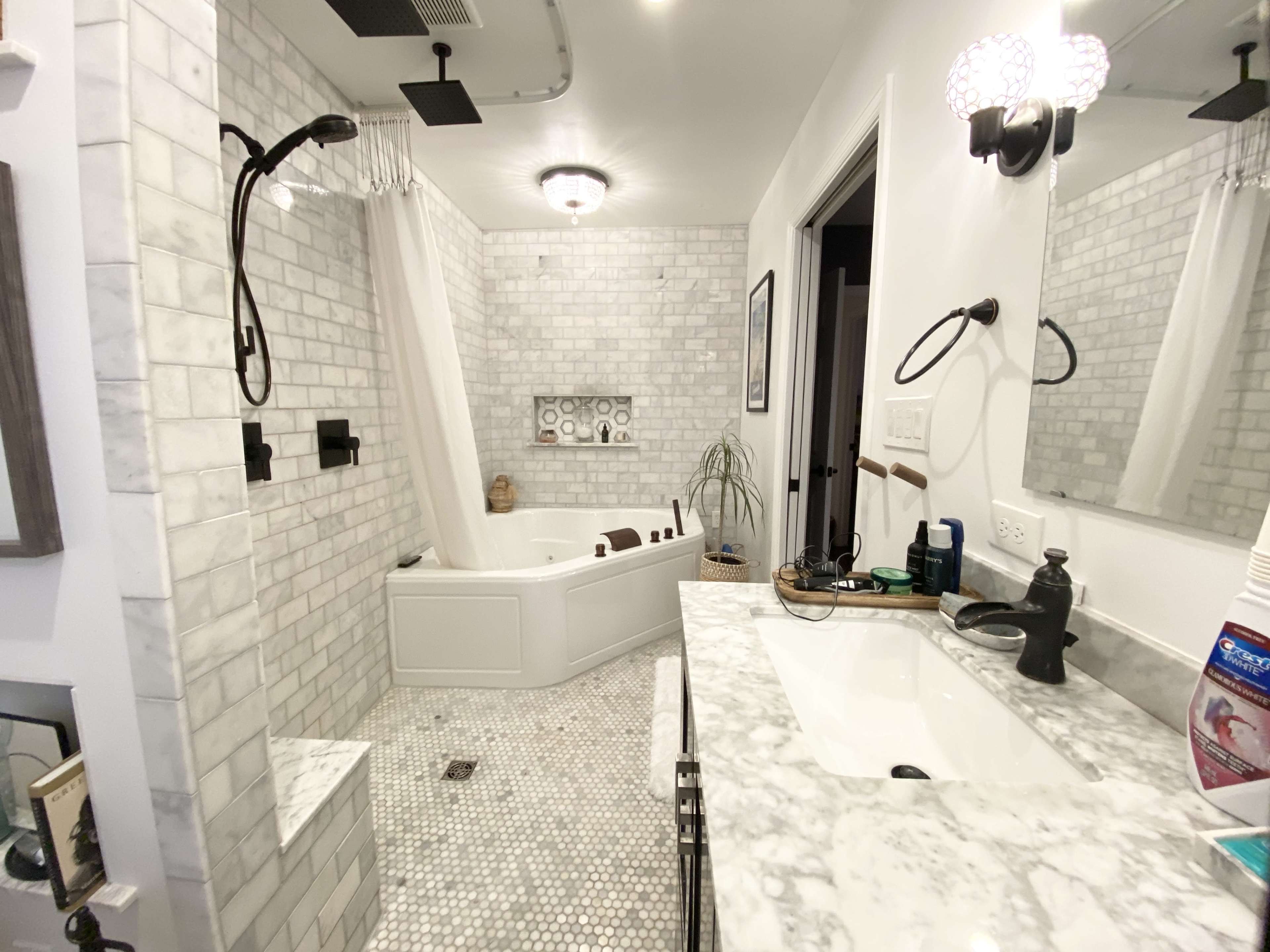 The image shows a modern bathroom featuring a marble countertop, a freestanding bathtub, a walk-in shower with black fixtures, and a tiled wall.