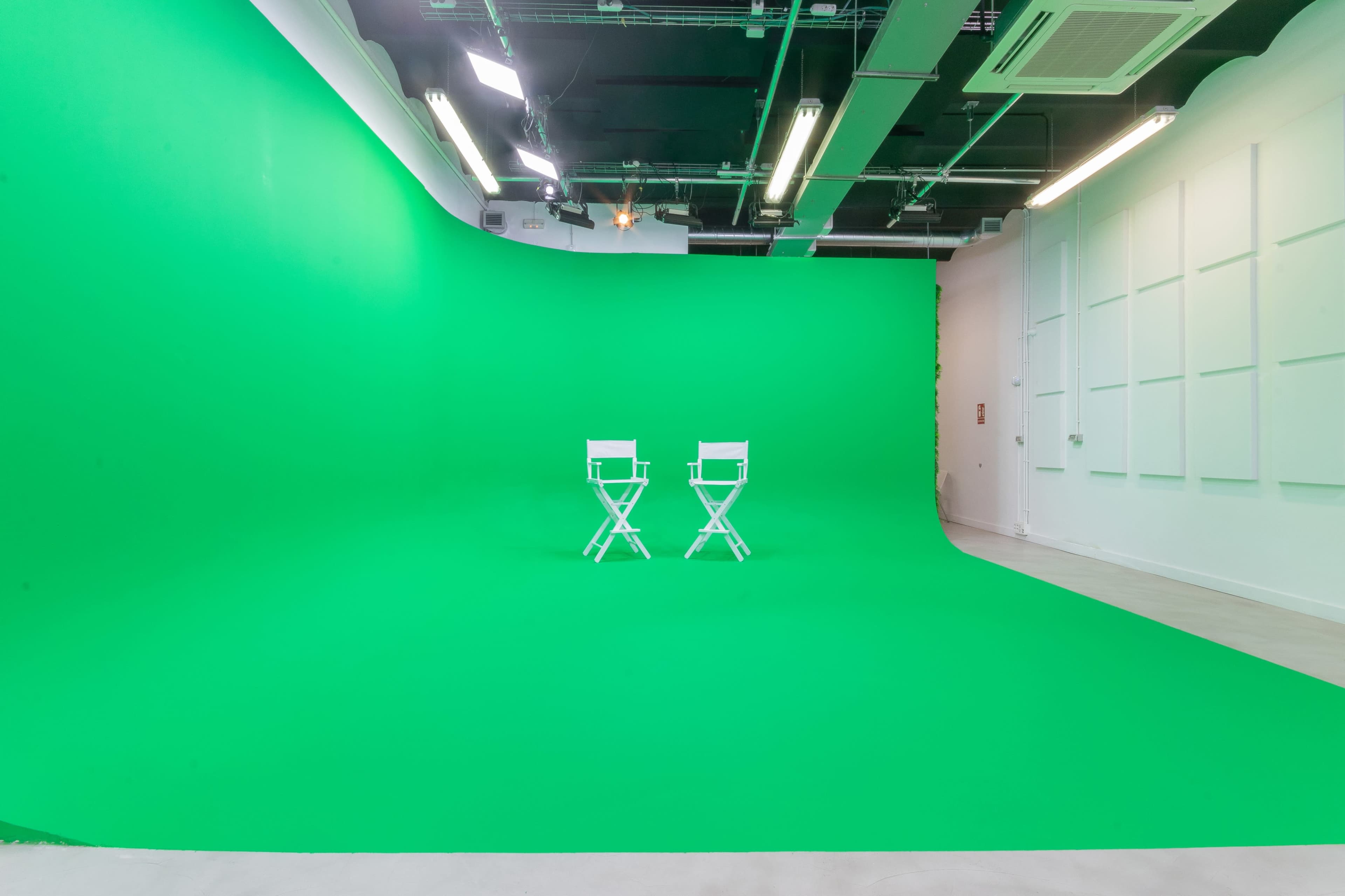 A photography studio featuring a curved green backdrop and two white director's chairs positioned in front.
