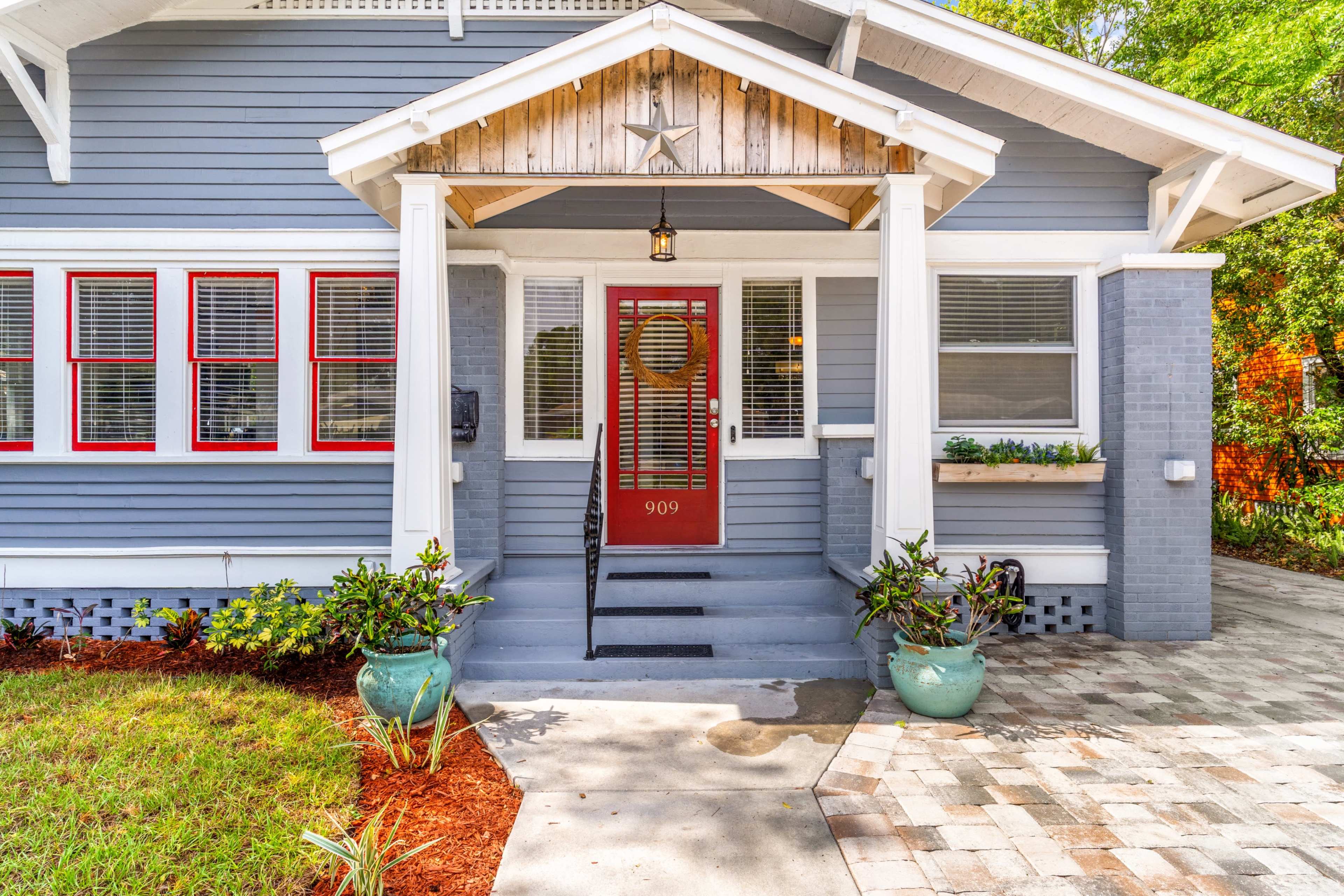 A gray house with red-trimmed windows and a covered front porch featuring a decorative star and a welcoming wreath on the door.