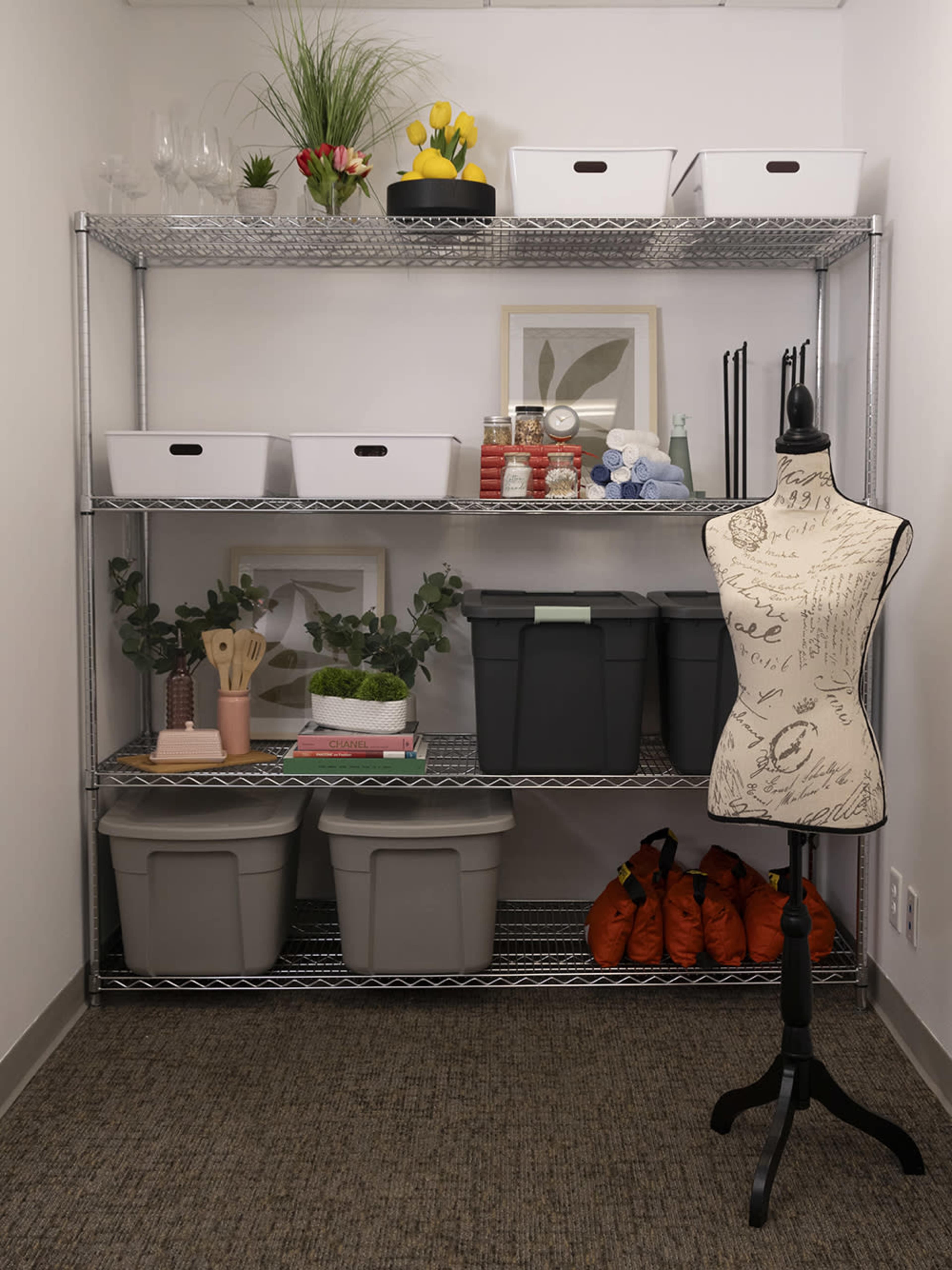 A metal shelving unit holds various storage bins, kitchen items, and decorative plants in a neat, organized corner of a room.