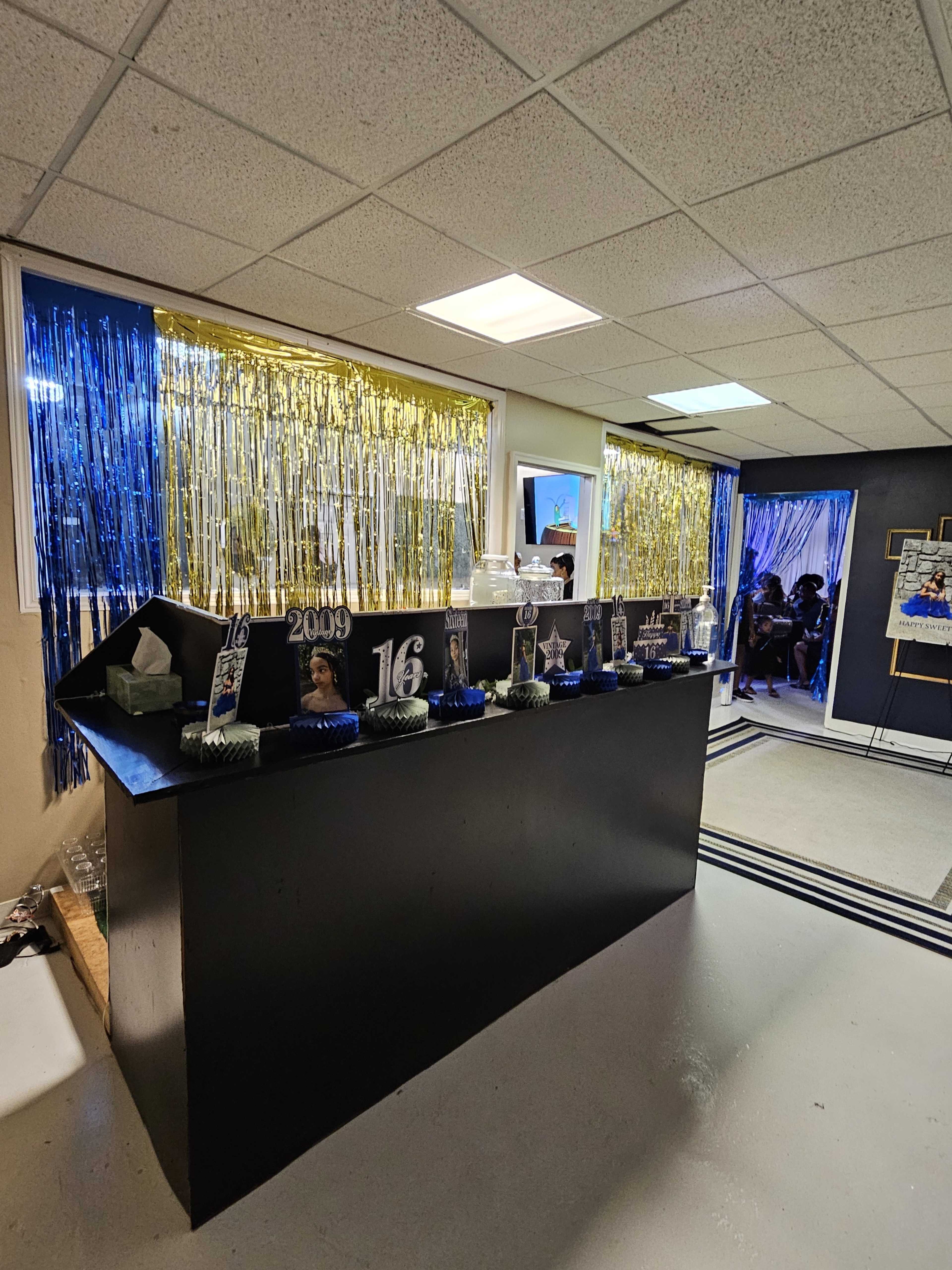 The image shows a decorated party space featuring a black bar with various 2009-themed items and a backdrop of blue and gold streamers.