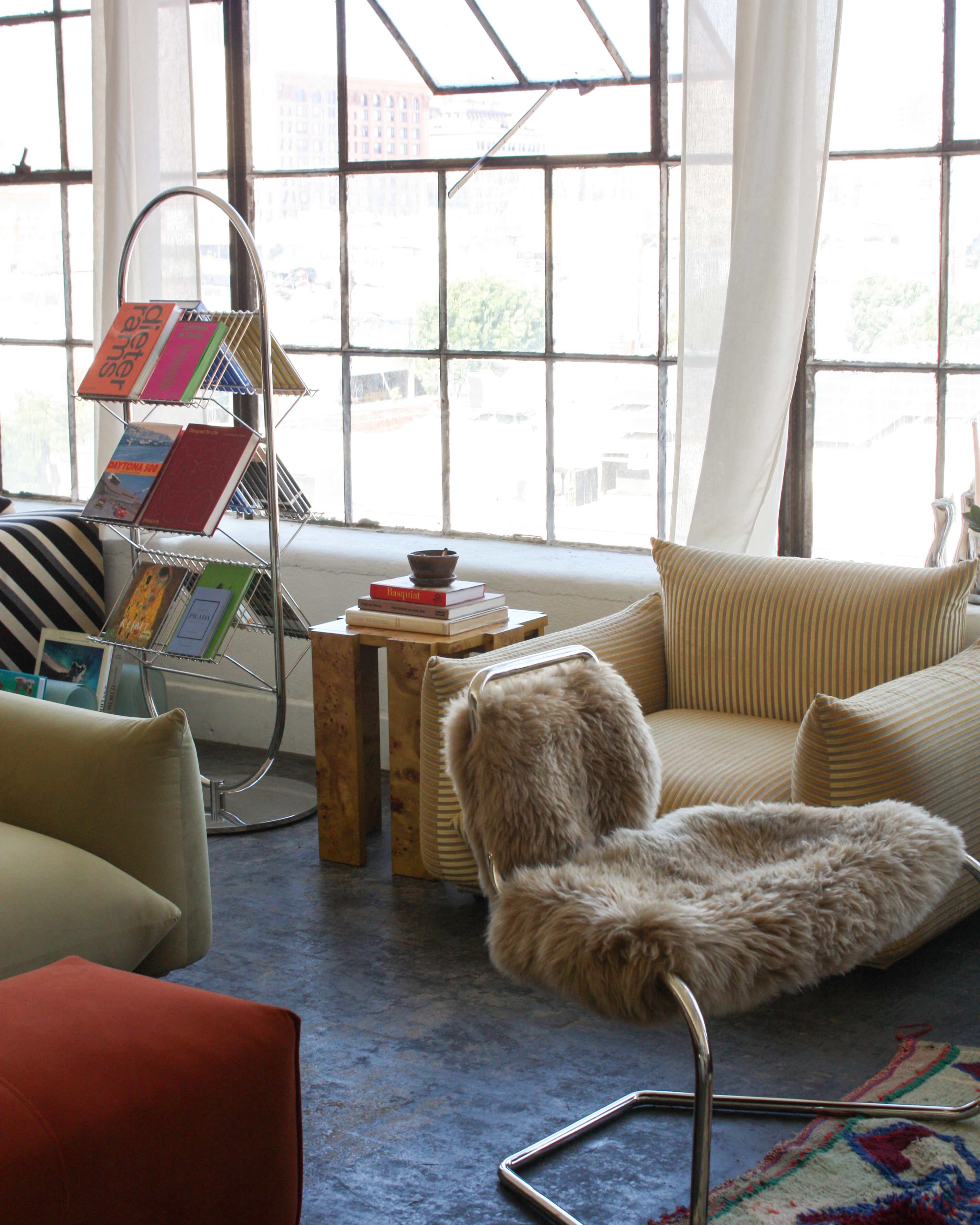 A cozy interior features a plush chair and a stylish reading nook with a circular bookshelf displaying colorful books next to large windows.