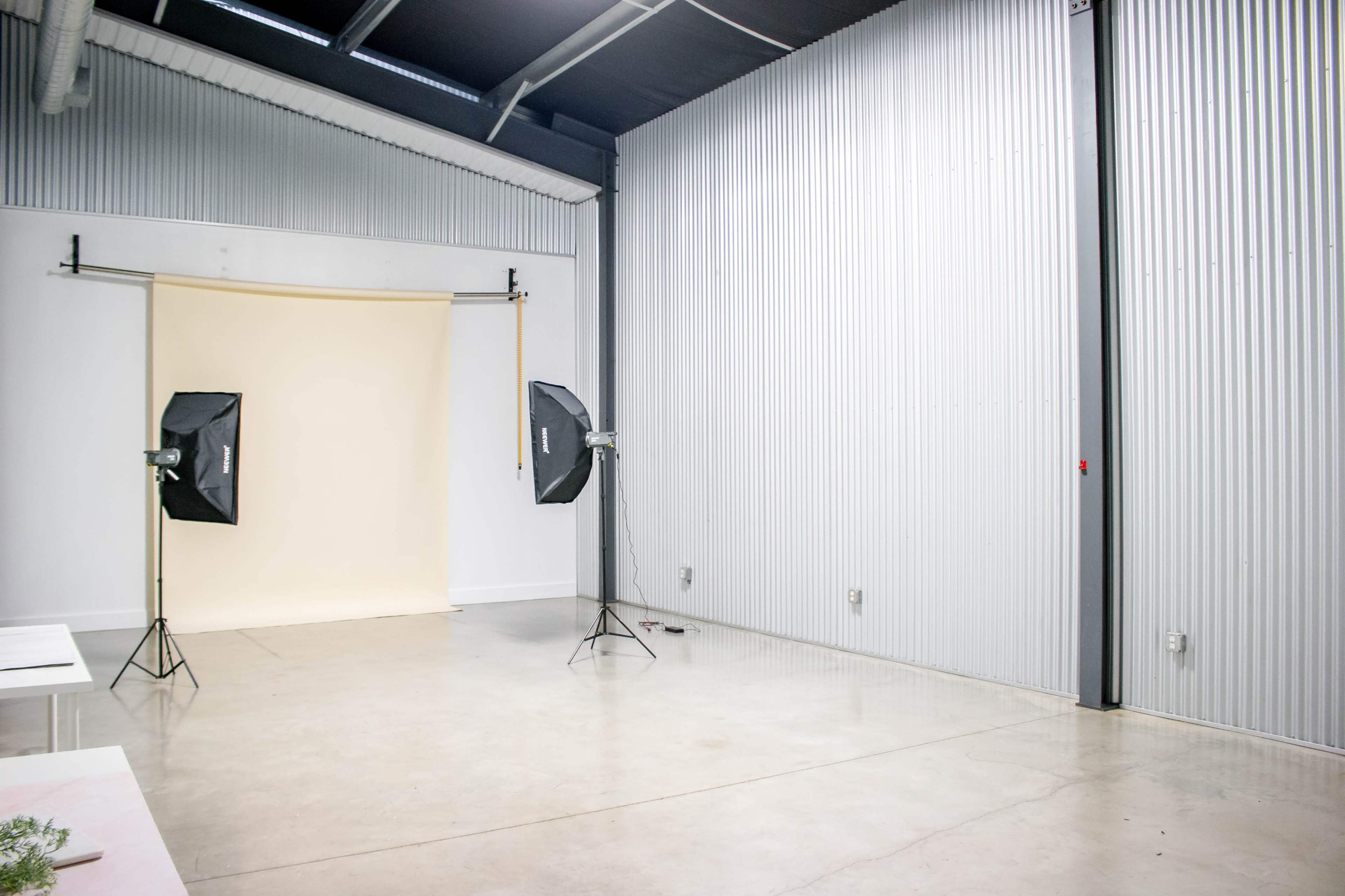 A photography studio with two softbox lights set up on either side of a beige backdrop against a corrugated metal wall.