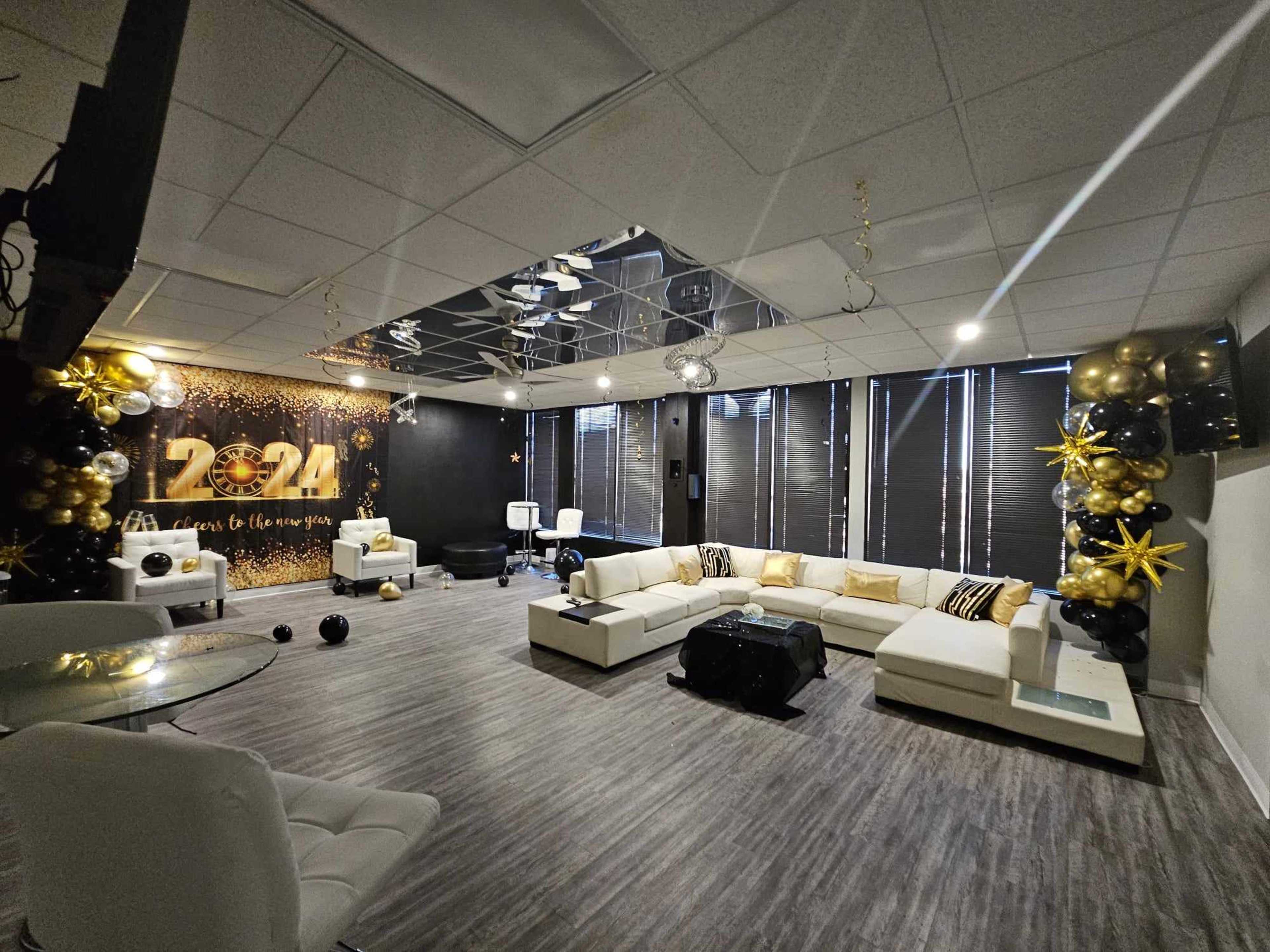 A modern event space decorated with black and gold balloons, featuring a white seating area and a wall adorned with "2024" in large numerals.