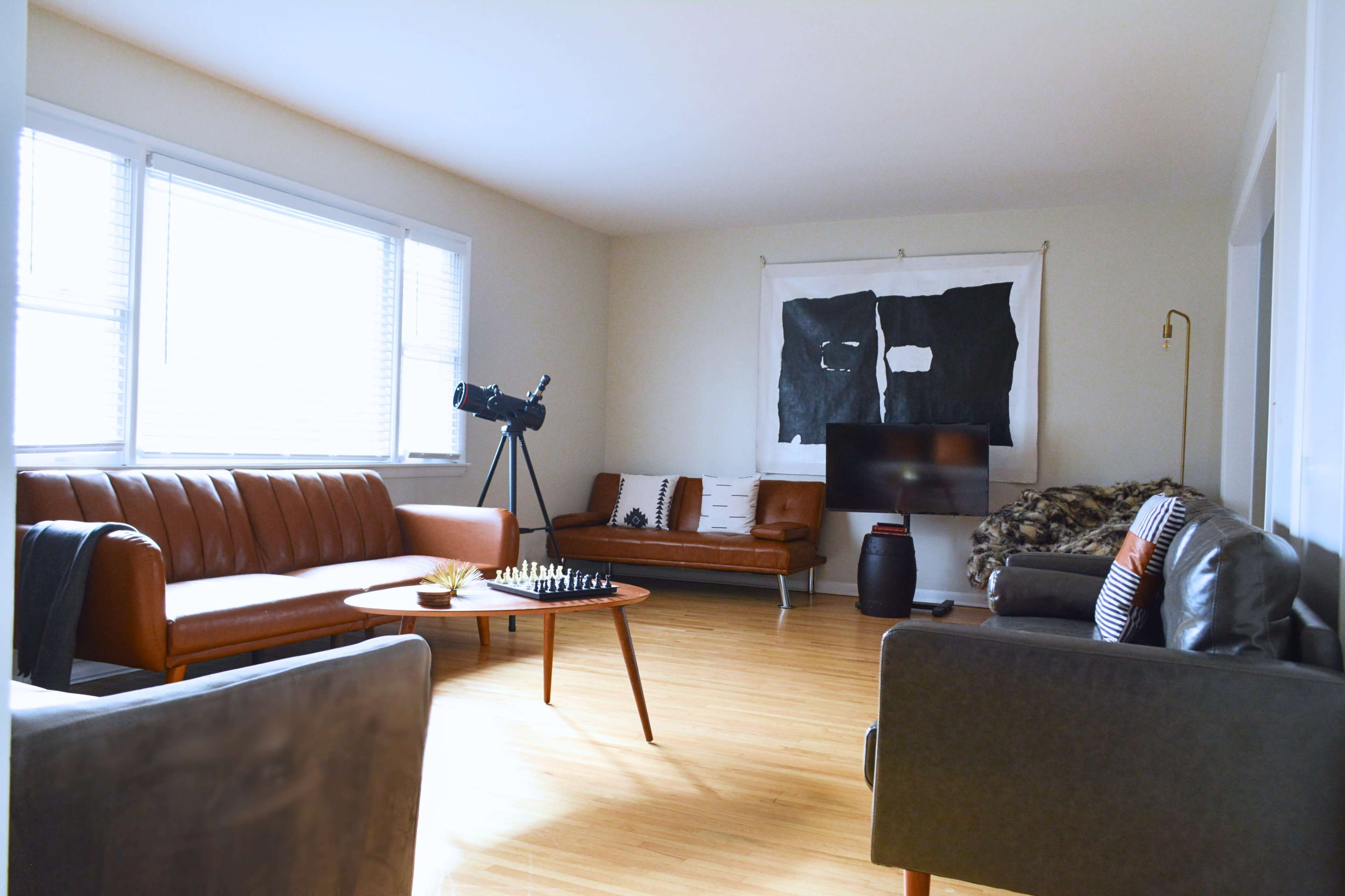 The living room features two leather sofas, a telescope by the window, a coffee table with a chess set, and a large artwork on the wall.