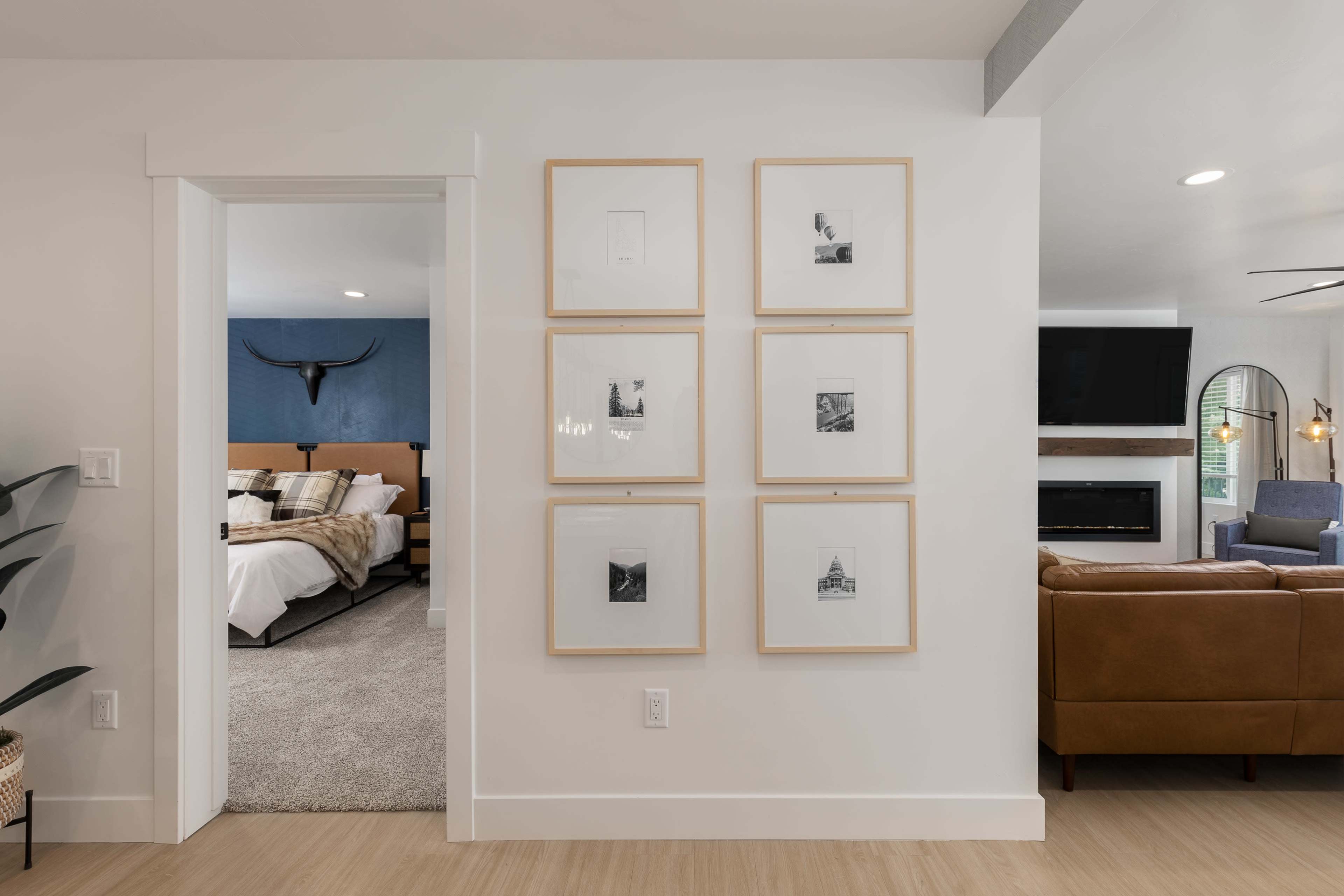 A modern hallway featuring a grid of six framed artworks on the wall, leading to a bedroom with a blue accent wall in the background.