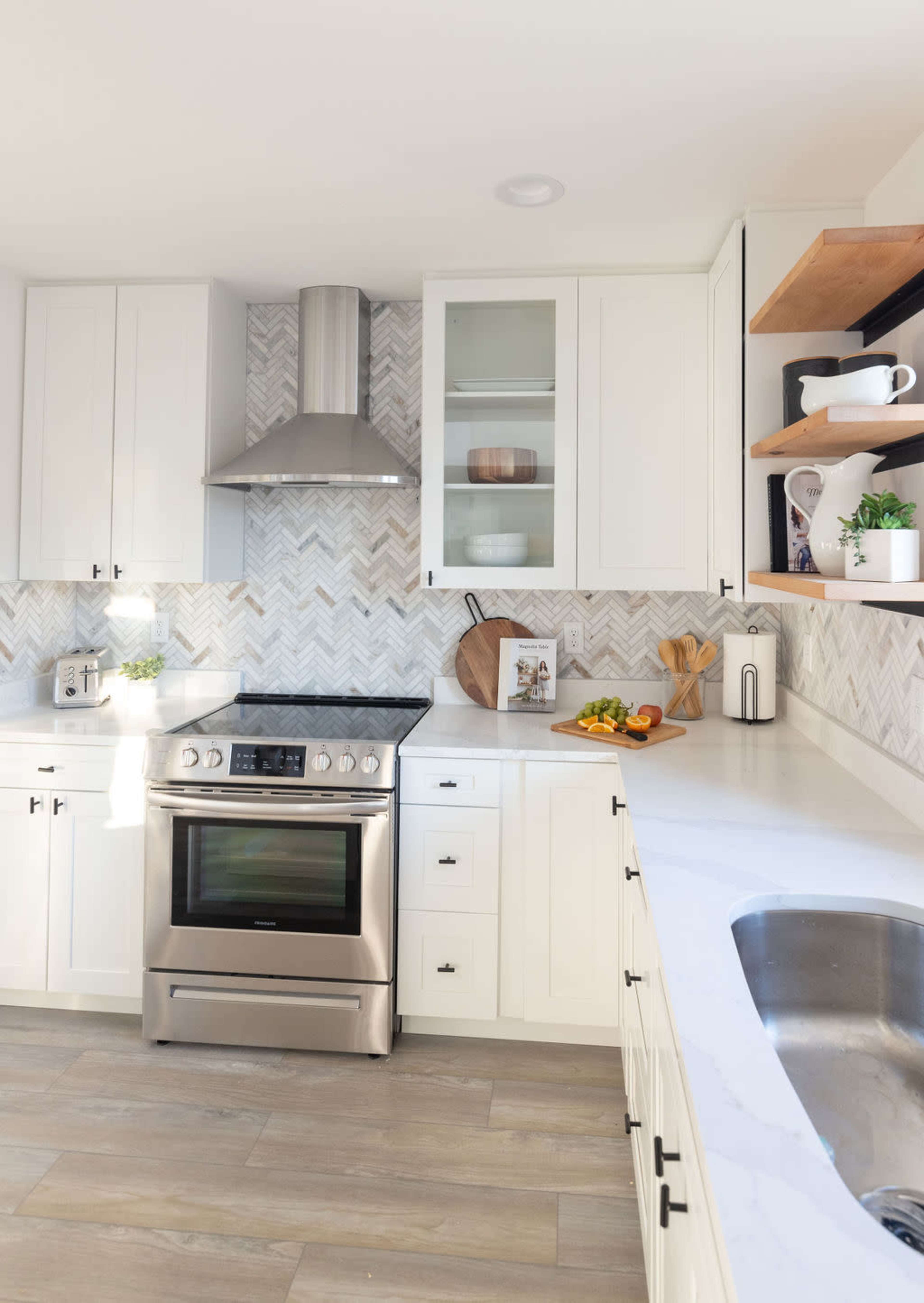 A modern kitchen featuring white cabinetry, a stainless steel stove, and a herringbone patterned backsplash.