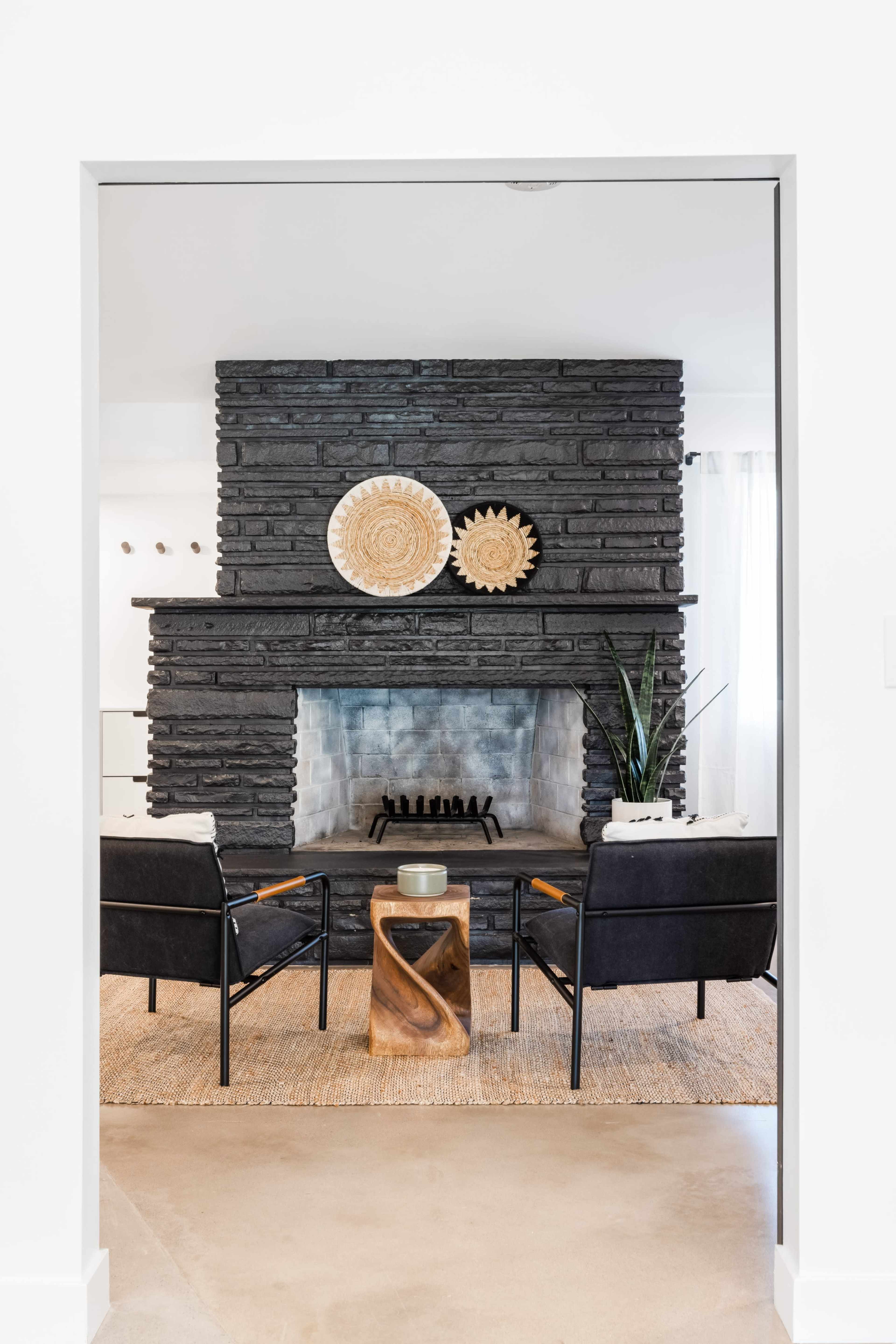 A modern living room features a stone fireplace, two chairs, and a coffee table, framed by a doorway.