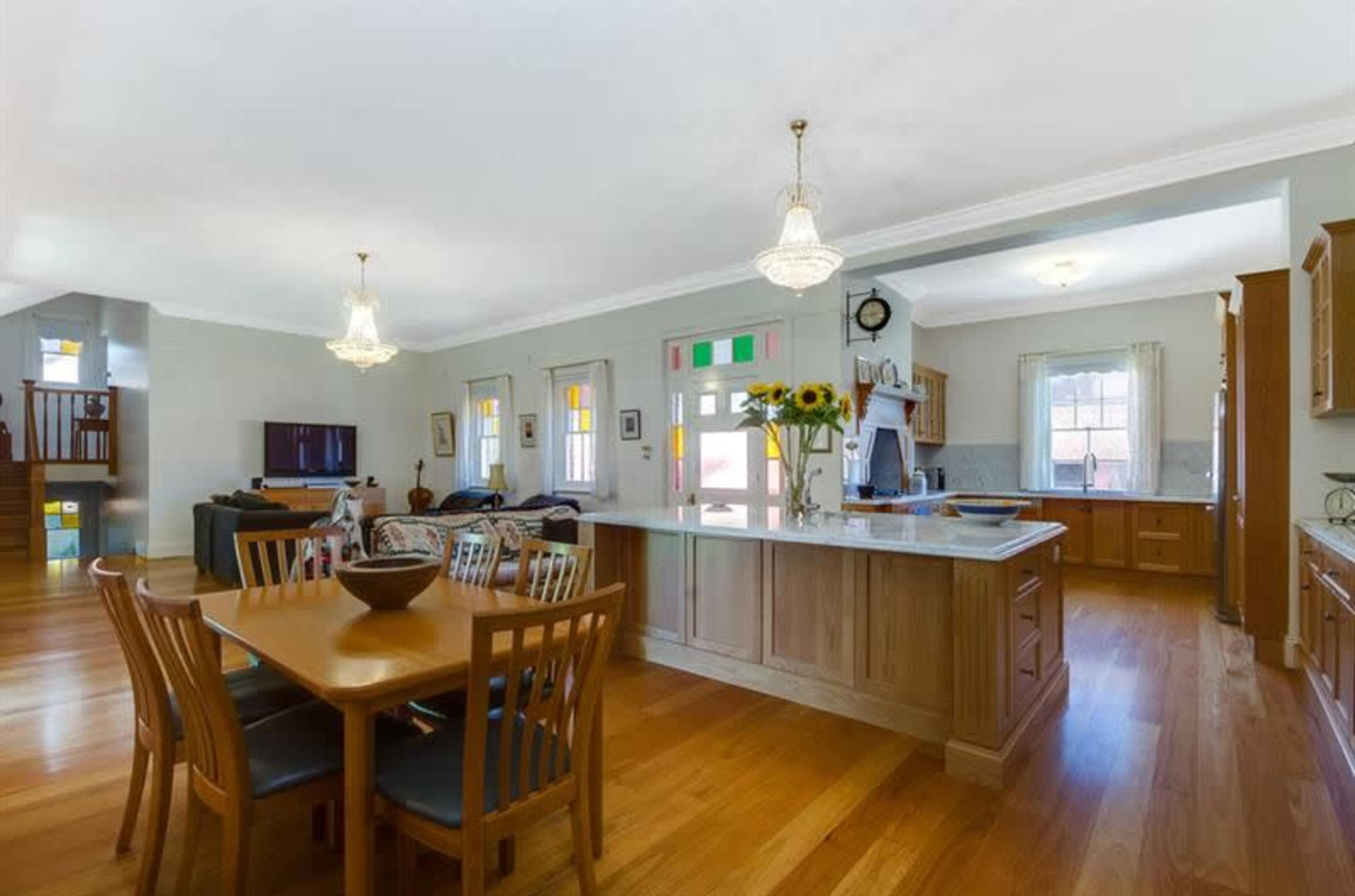 The image shows a spacious open-concept kitchen and dining area, featuring wooden floors, a large dining table, and a kitchen island.