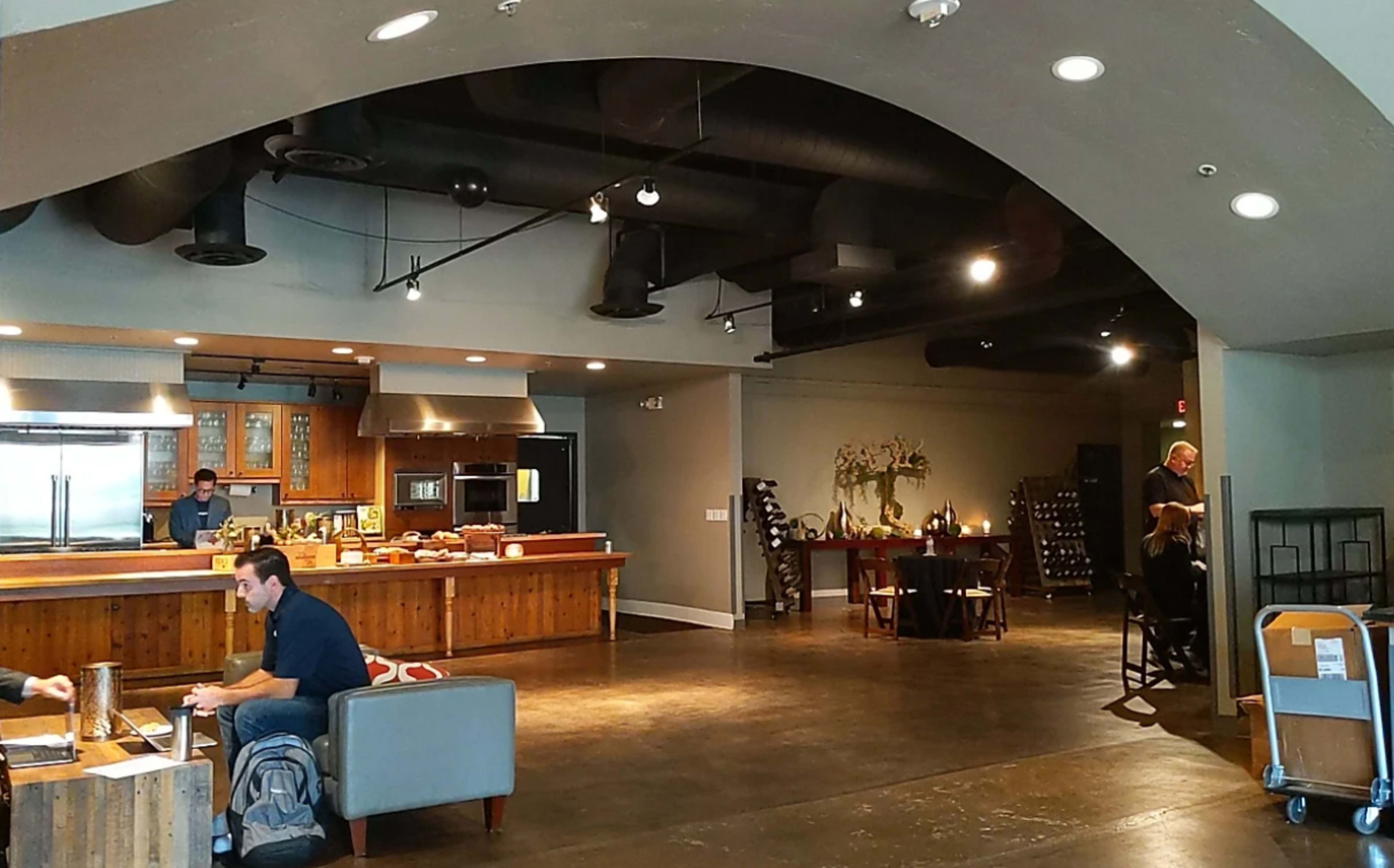 The image depicts an open interior space with a kitchen area, dining table, and seating arrangements.