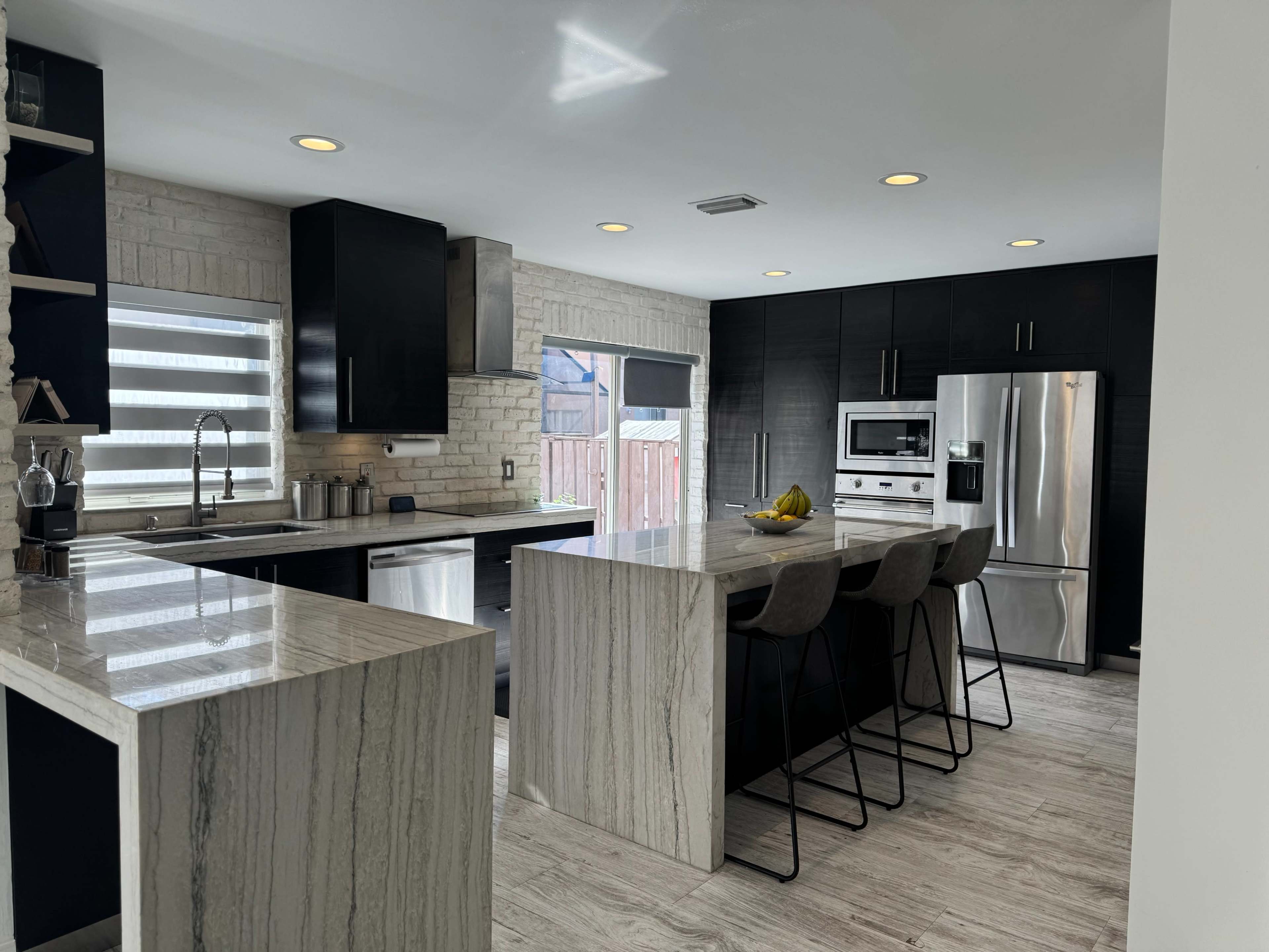 The image shows a modern kitchen featuring dark cabinetry, light countertops, and a large island with seating for four.