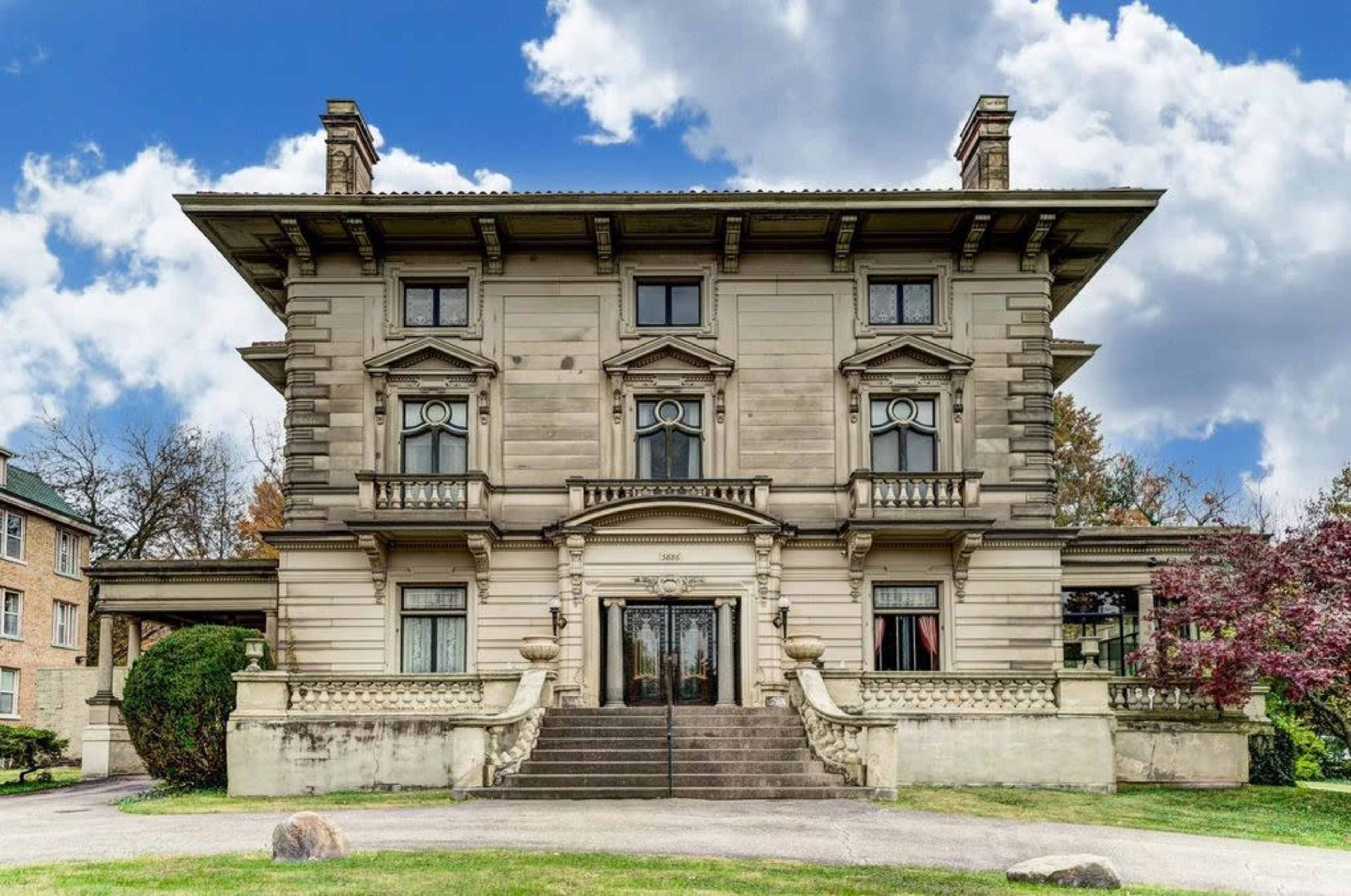 A large, ornate mansion with a symmetrical facade, featuring multiple windows and a grand entrance flanked by stairs.