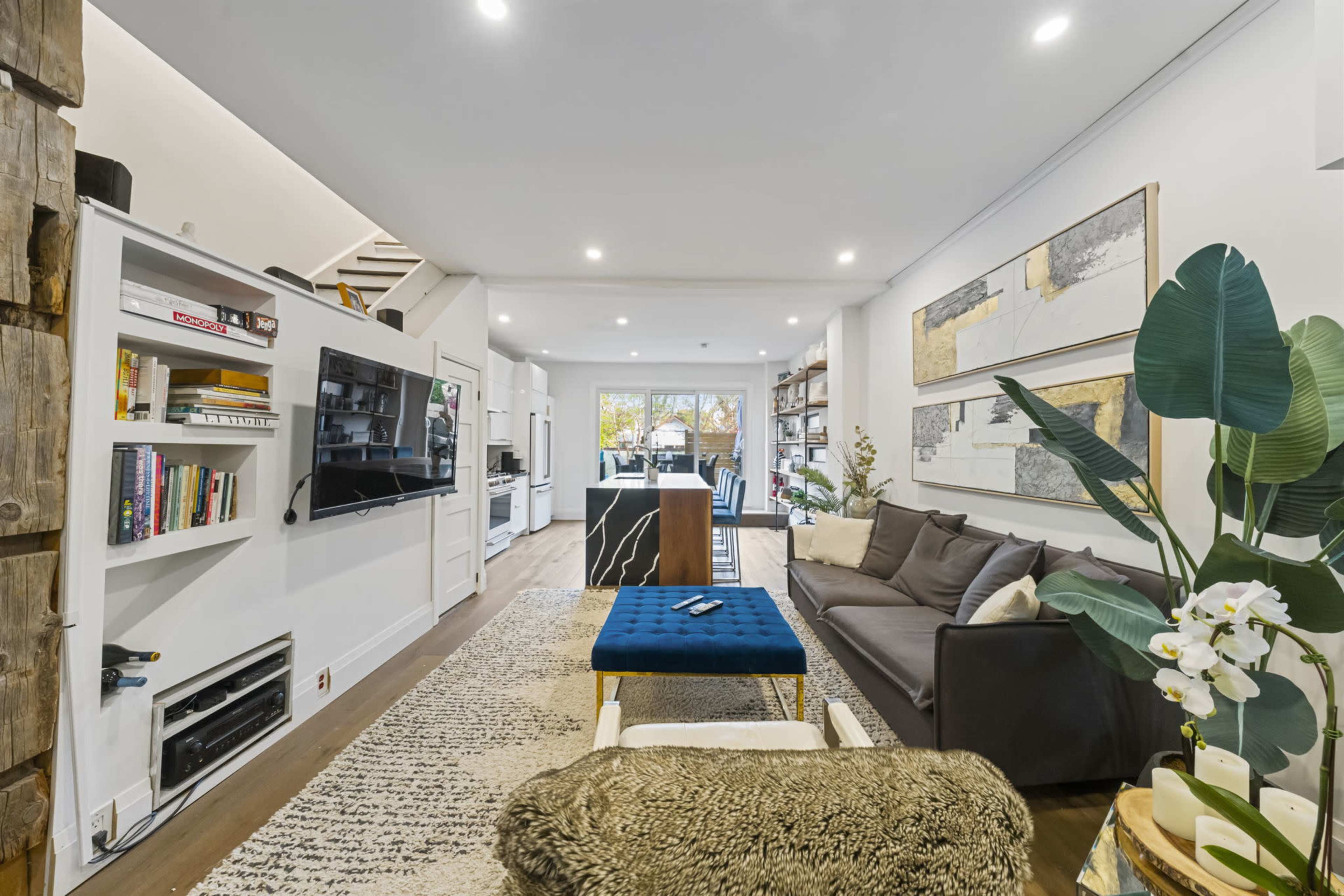 A modern living room with a sofa, a coffee table, shelves filled with books, and a view toward a dining area in the background.