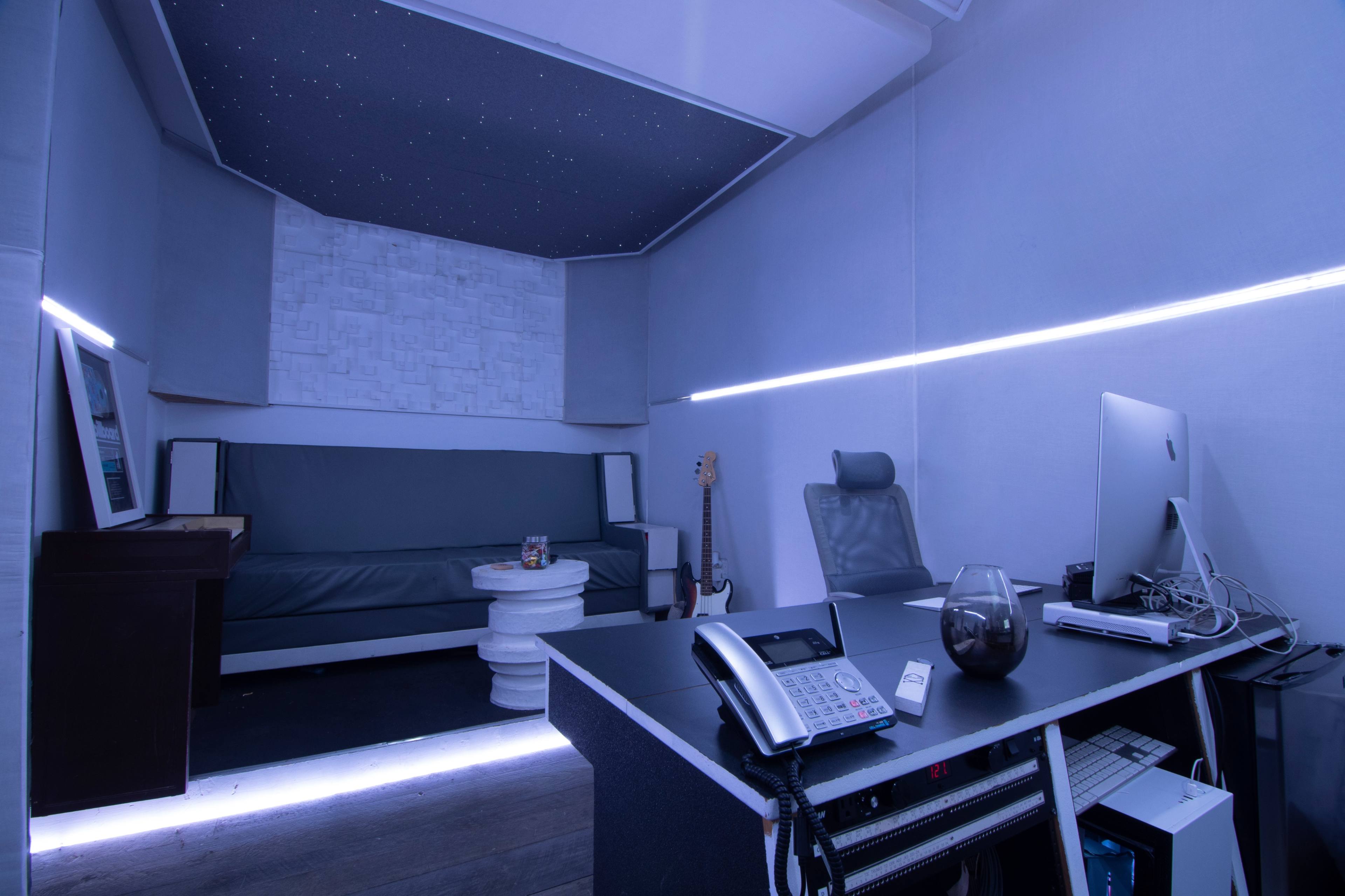 A modern office space featuring a desk with a computer, a telephone, and a round white table surrounded by a couch and a guitar.