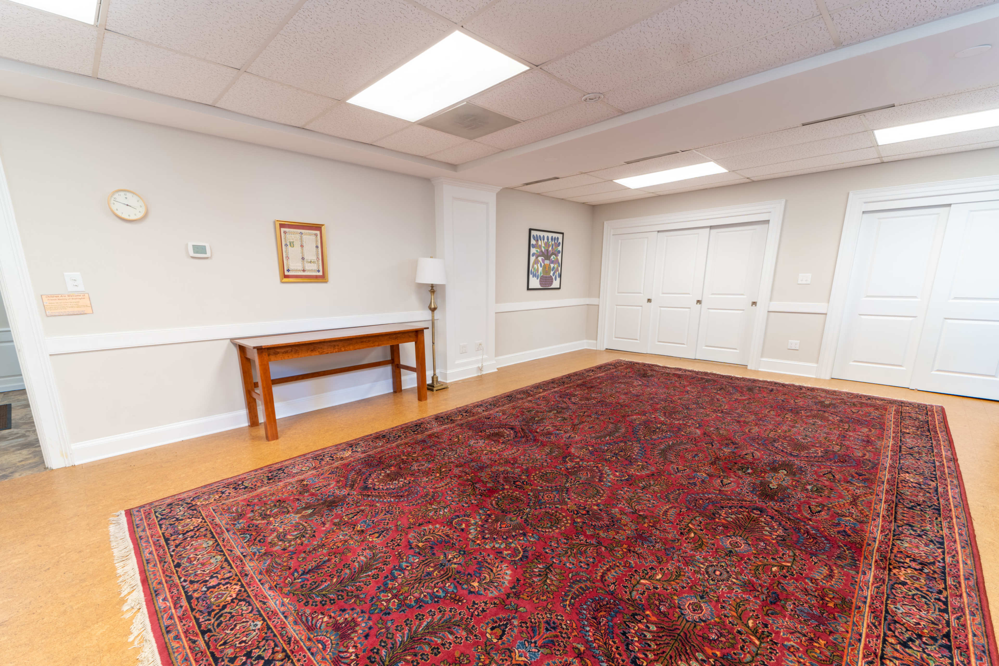 A spacious room with a large patterned rug, a wooden table with a lamp, and two sets of closed double doors.