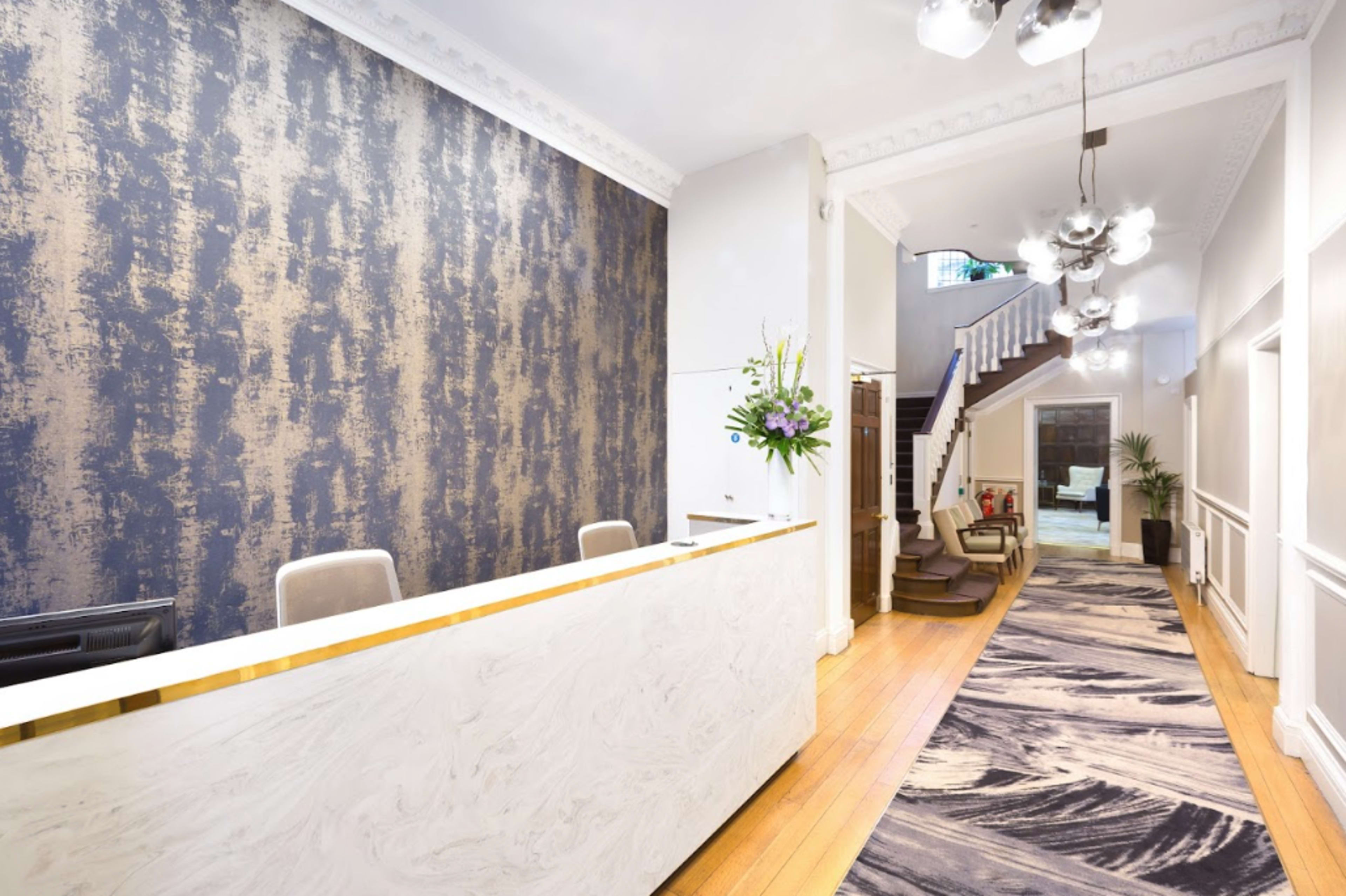 A modern reception area with a marble desk, a decorative wall, and a staircase leading to the upper floor.