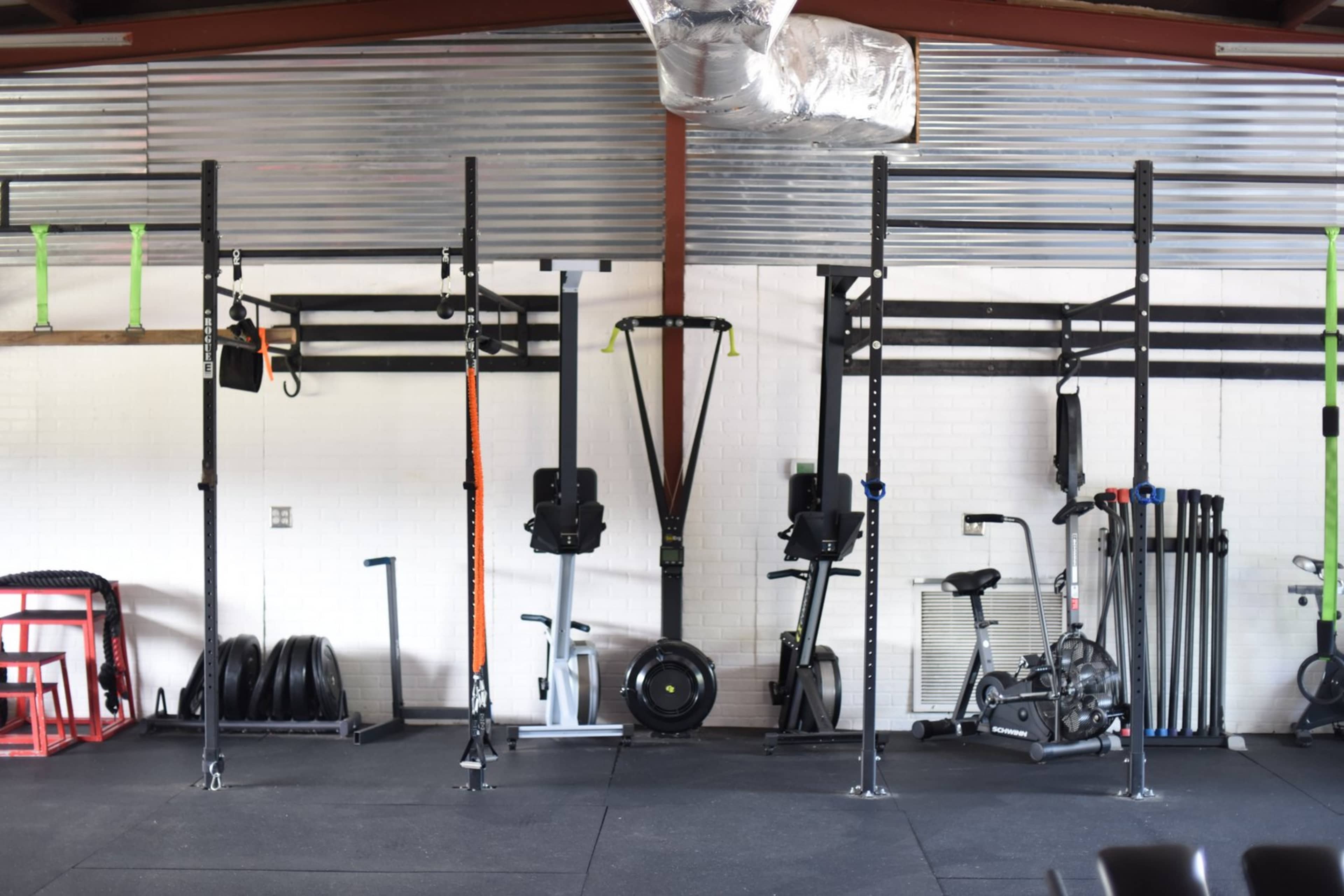 A gym interior with various gym equipment including squat racks, rowing machines, resistance bands, weights, and a stationary bike.