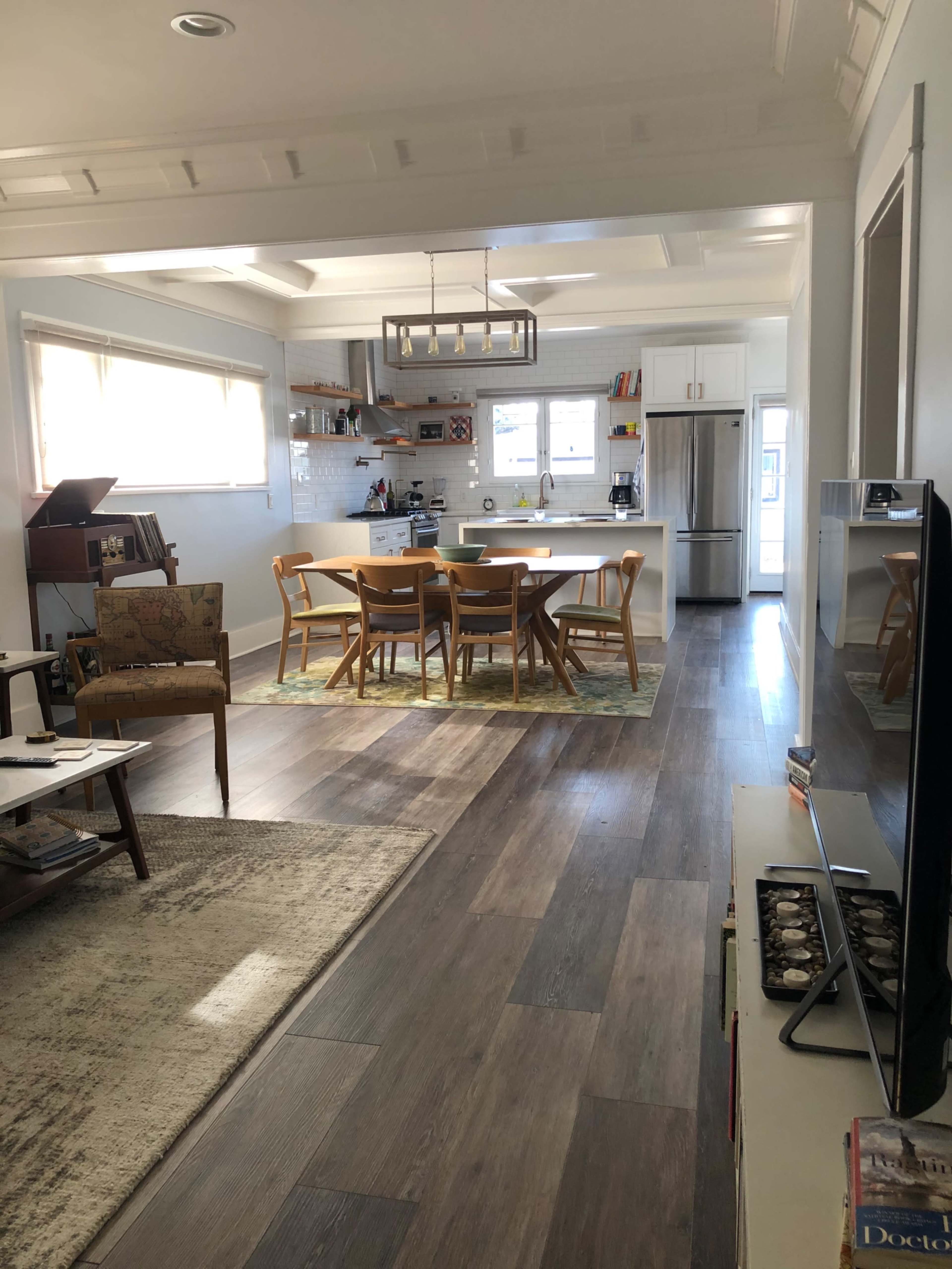 The image shows a modern kitchen and dining area, featuring a table with four chairs, hardwood flooring, and white cabinetry.