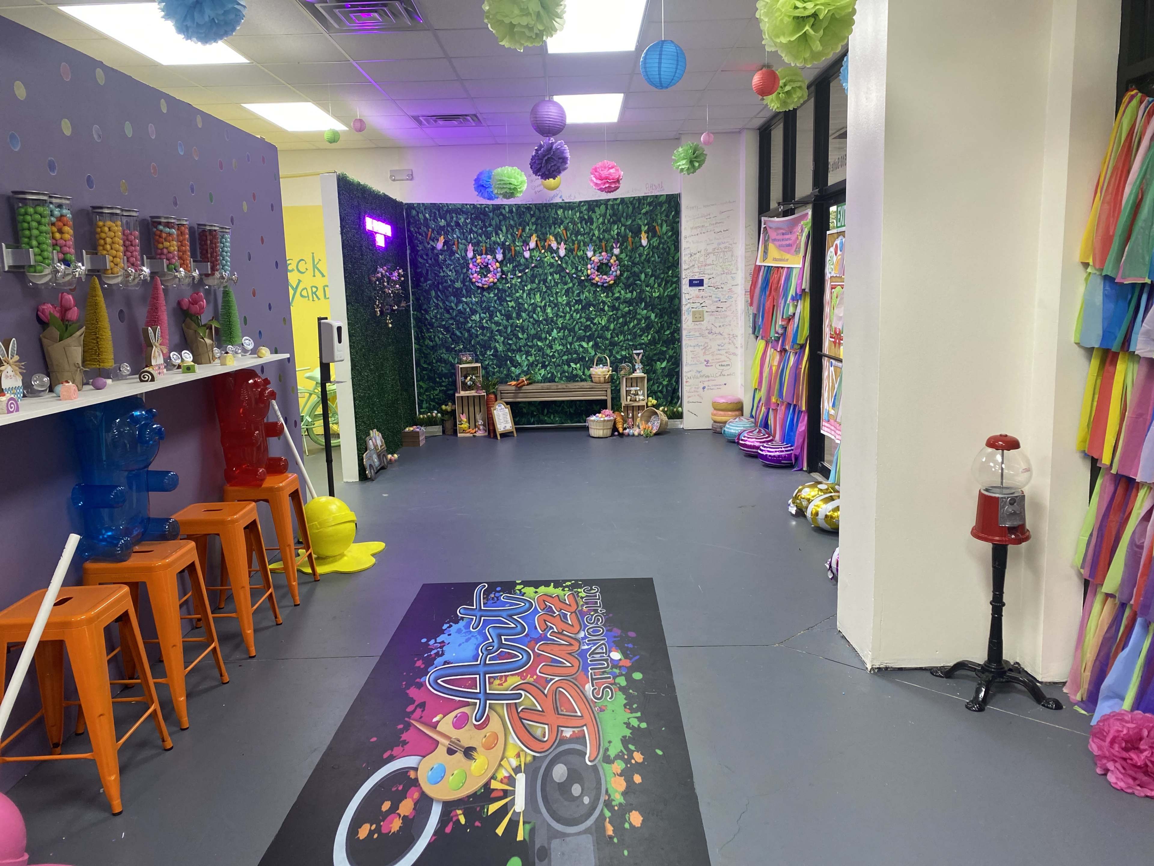 A colorful recreational space featuring a vibrant activity area, a snack bar with orange stools, and a backdrop of greenery along with various decorations.