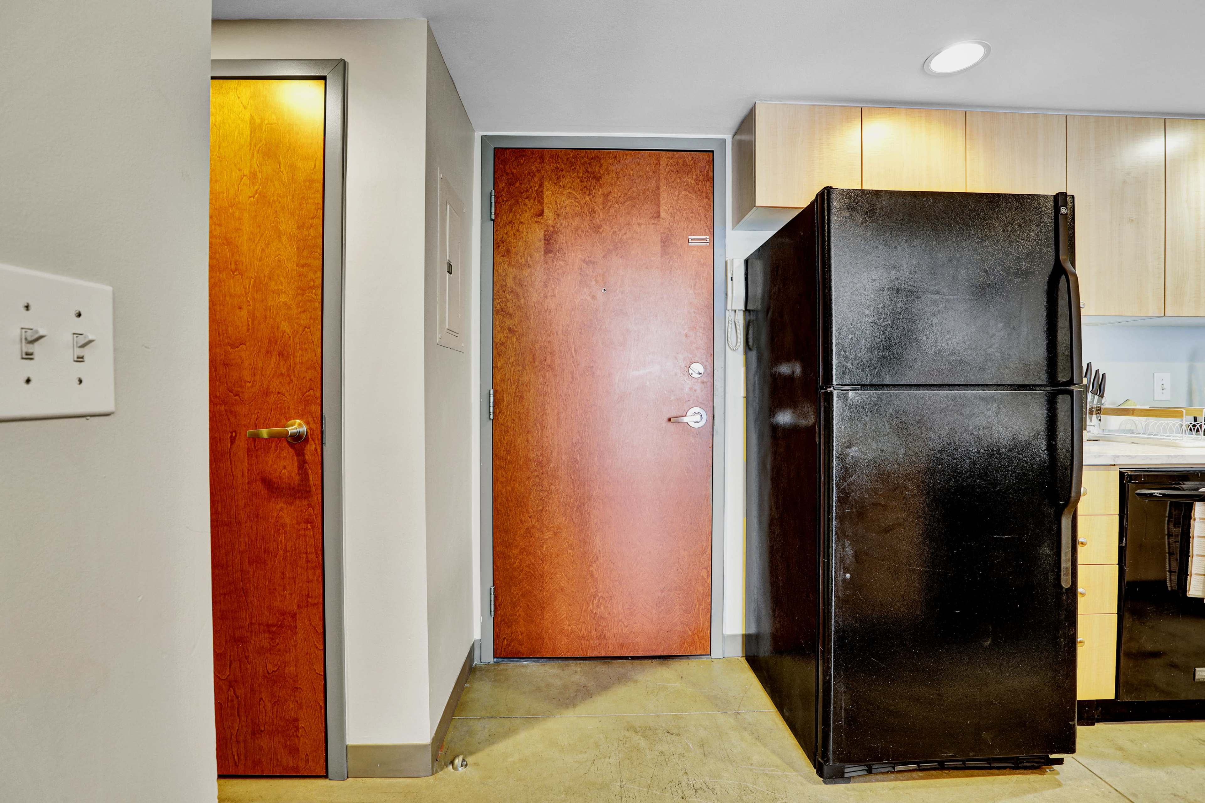 A kitchen area with a black refrigerator next to a wooden door and another door leading to a different room.