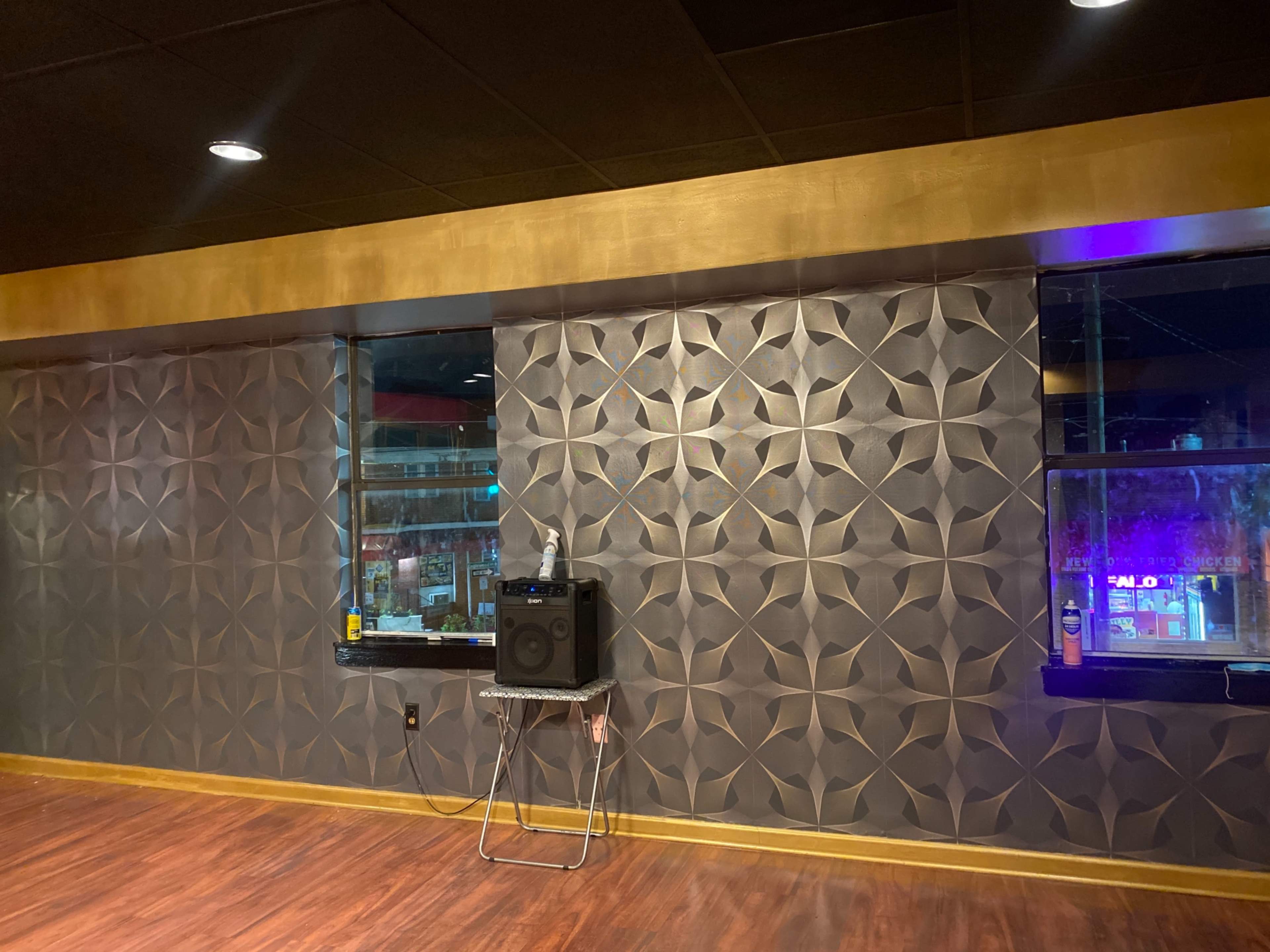 A room with a textured wall featuring a geometric design, two windows, and a speaker set on a folding table.