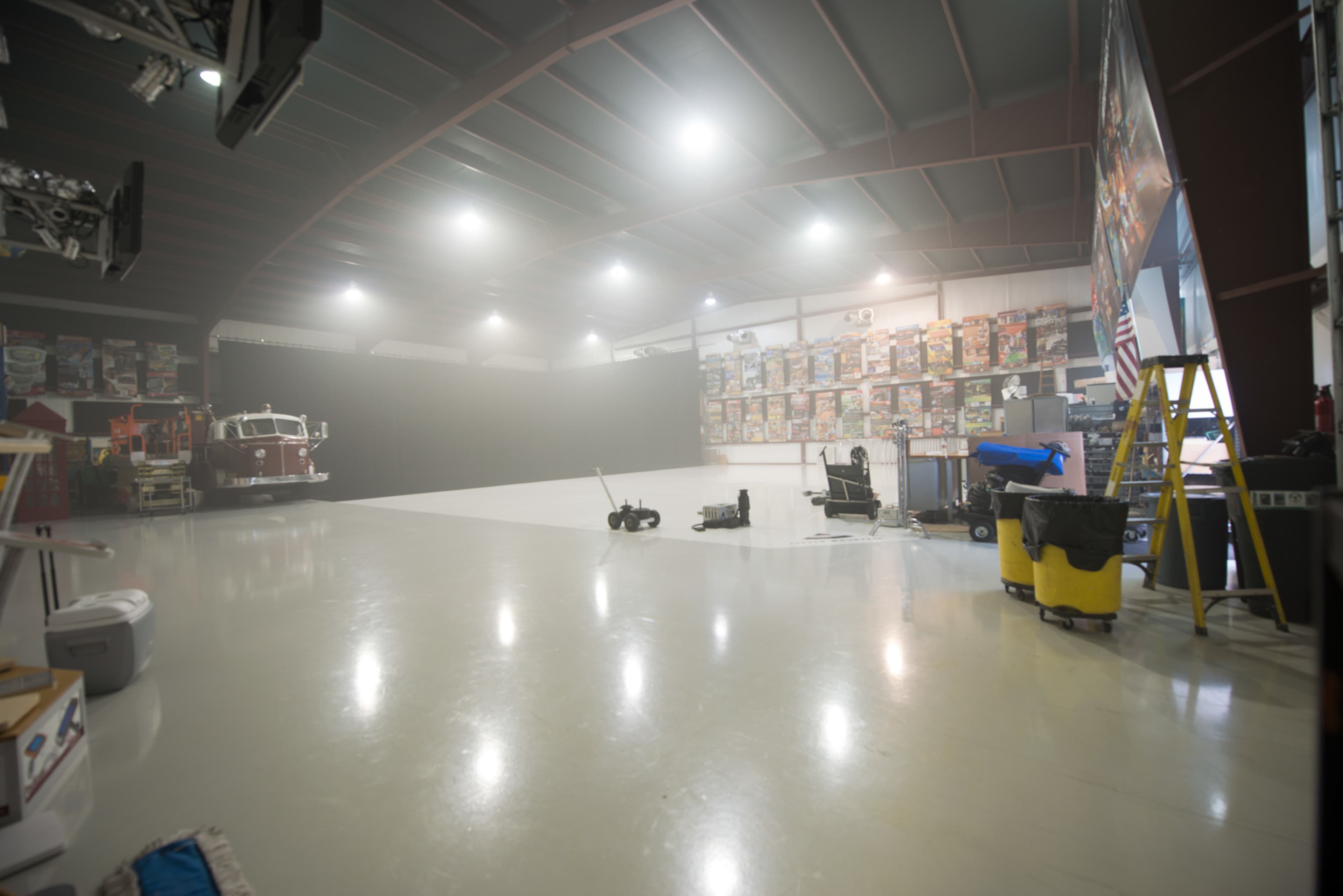 A spacious studio with a polished floor, featuring a black backdrop, scattered equipment, and walls adorned with colorful posters.