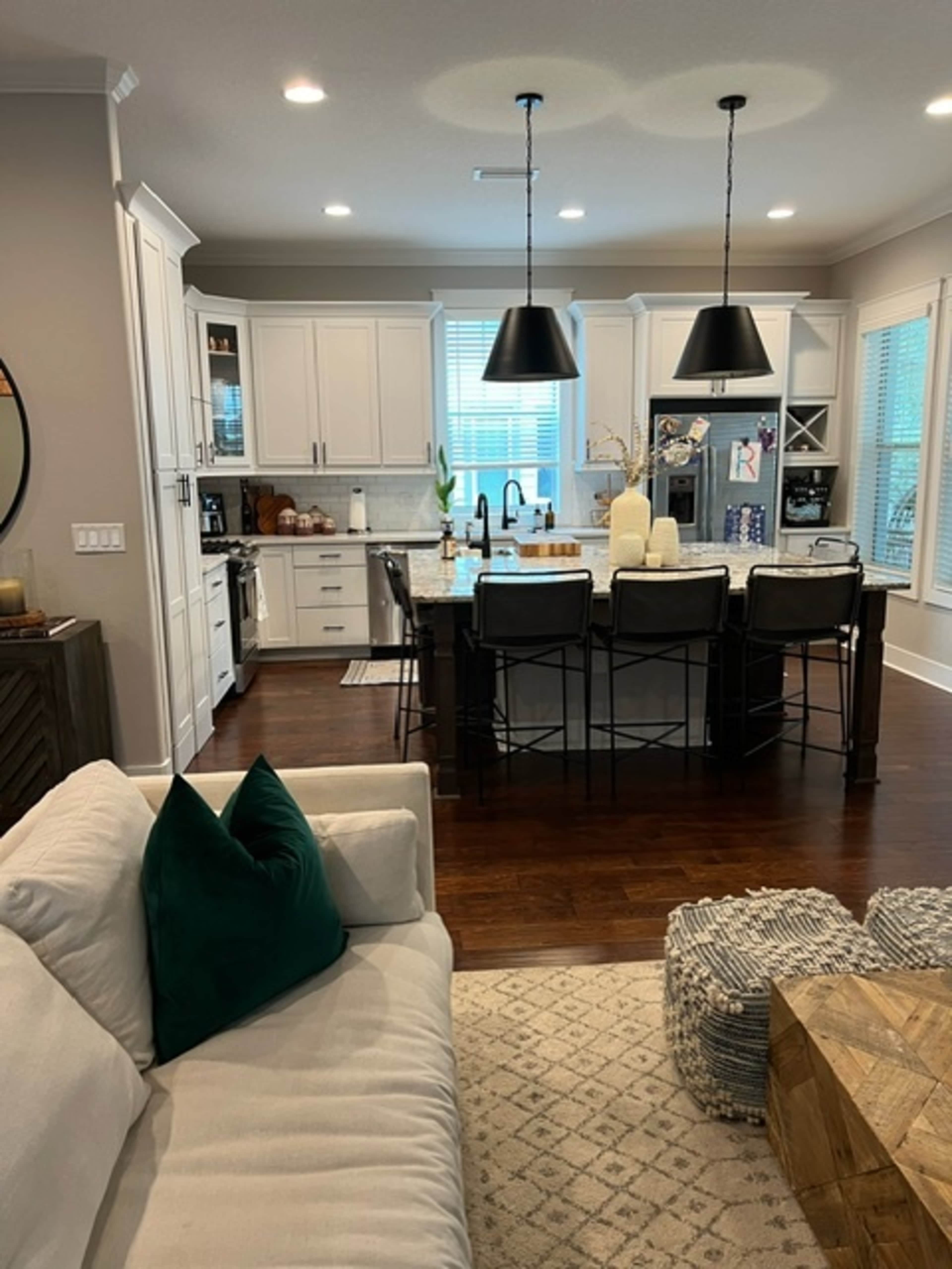 A modern kitchen features white cabinetry, dark pendant lights, and a large island with bar seating.