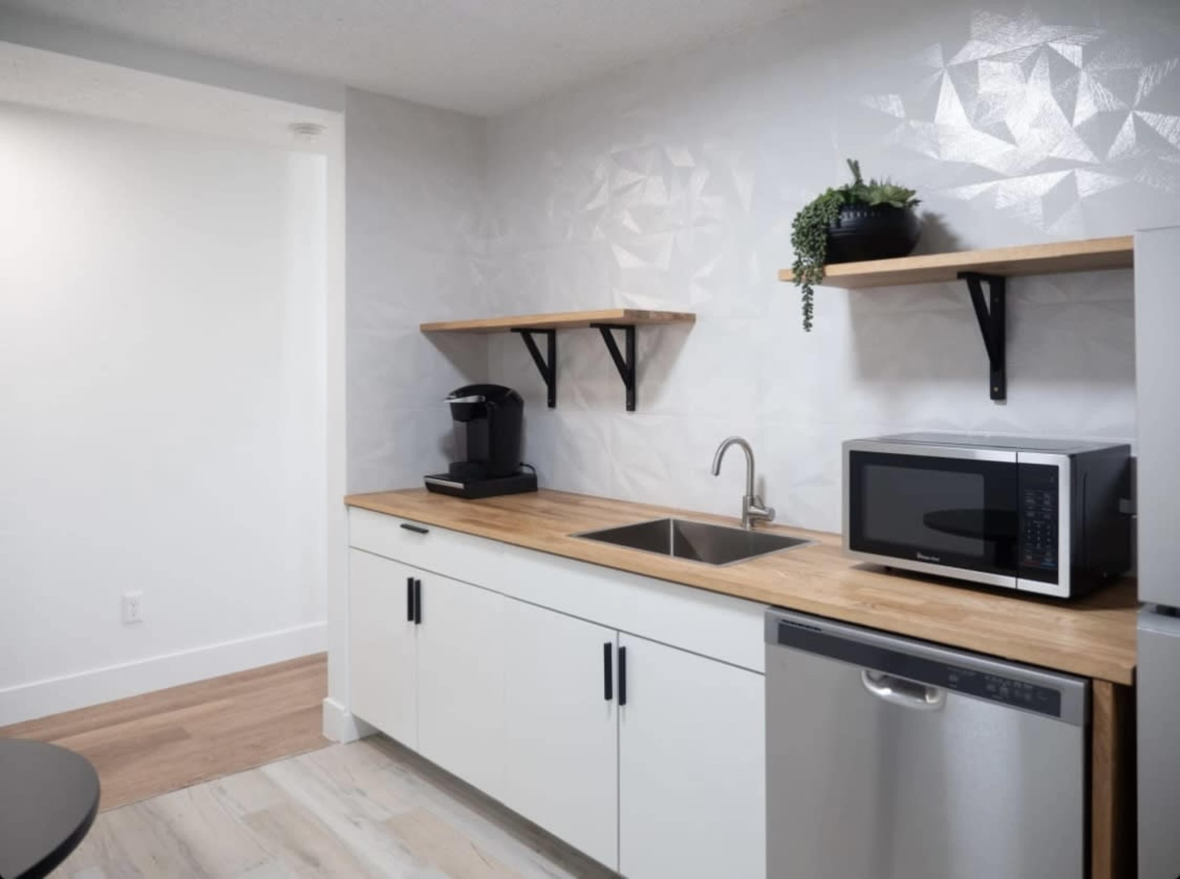 A modern kitchen with a wooden countertop, a sink, a microwave, a coffee machine, and open shelves for storage.