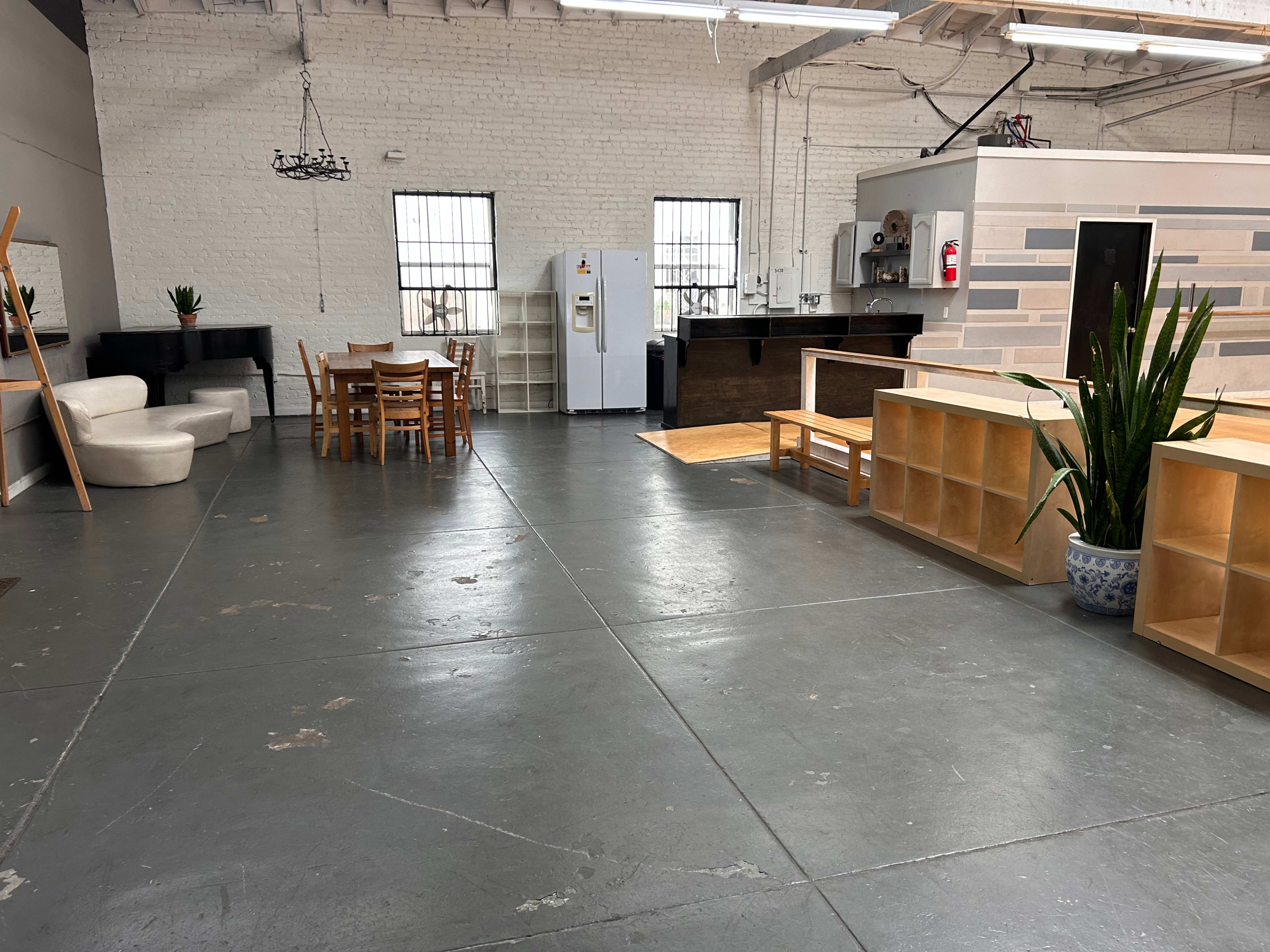 A spacious, industrial-style interior with a seating area, dining table, kitchen appliances, and shelving units.