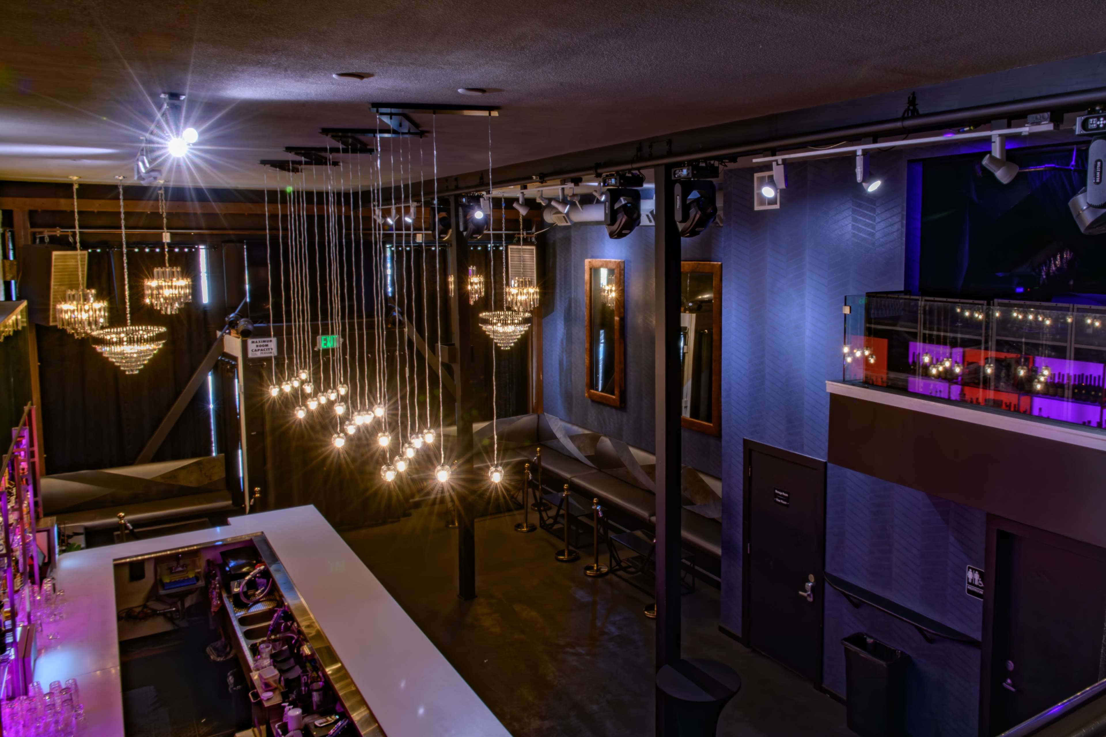 The image shows a modern bar interior with hanging light fixtures, a long white counter, and a seating area against the wall.