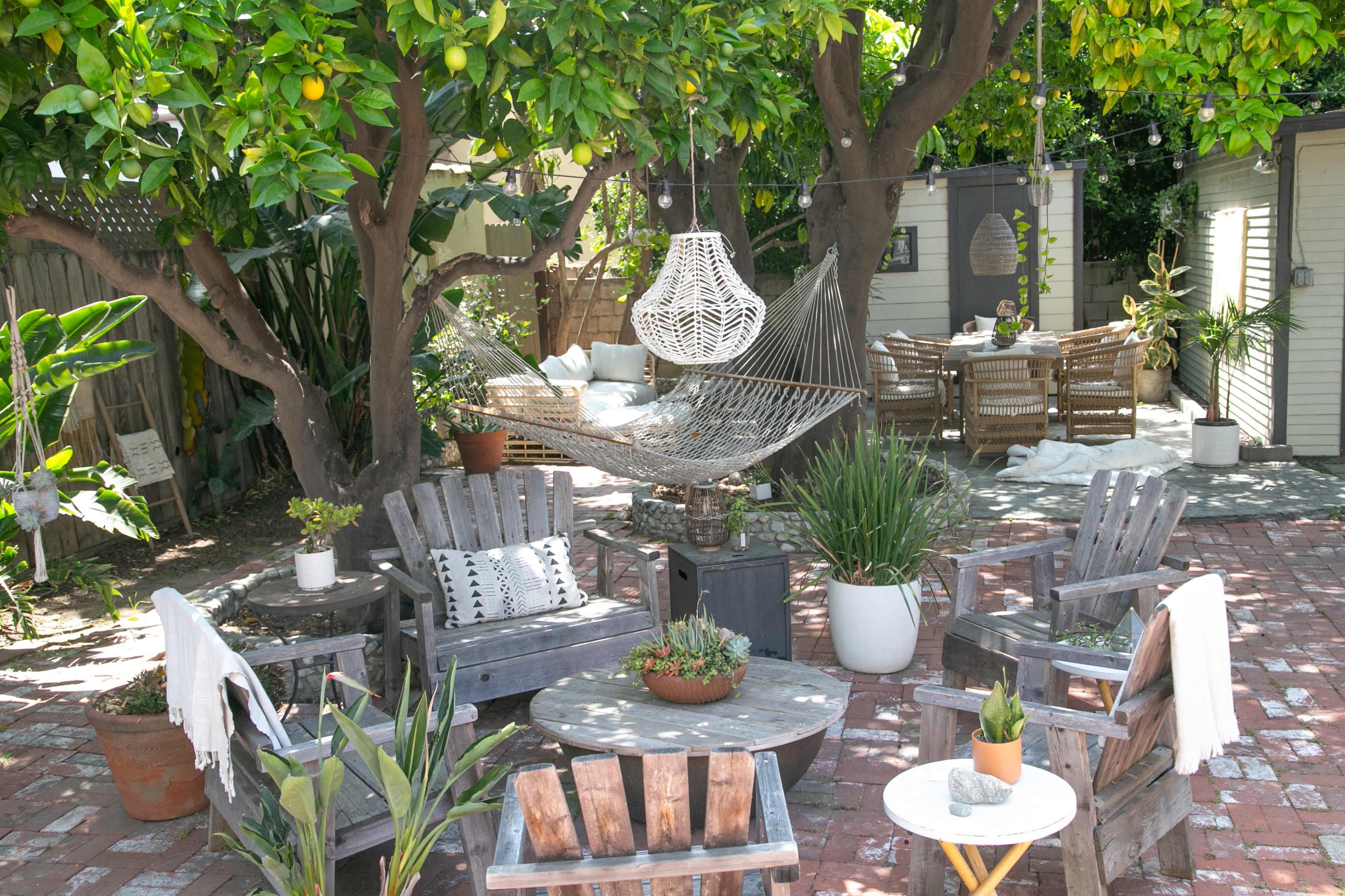 The outdoor area features a patio with wooden adirondack chairs, a hanging hammock, potted plants, and a dining table surrounded by greenery.