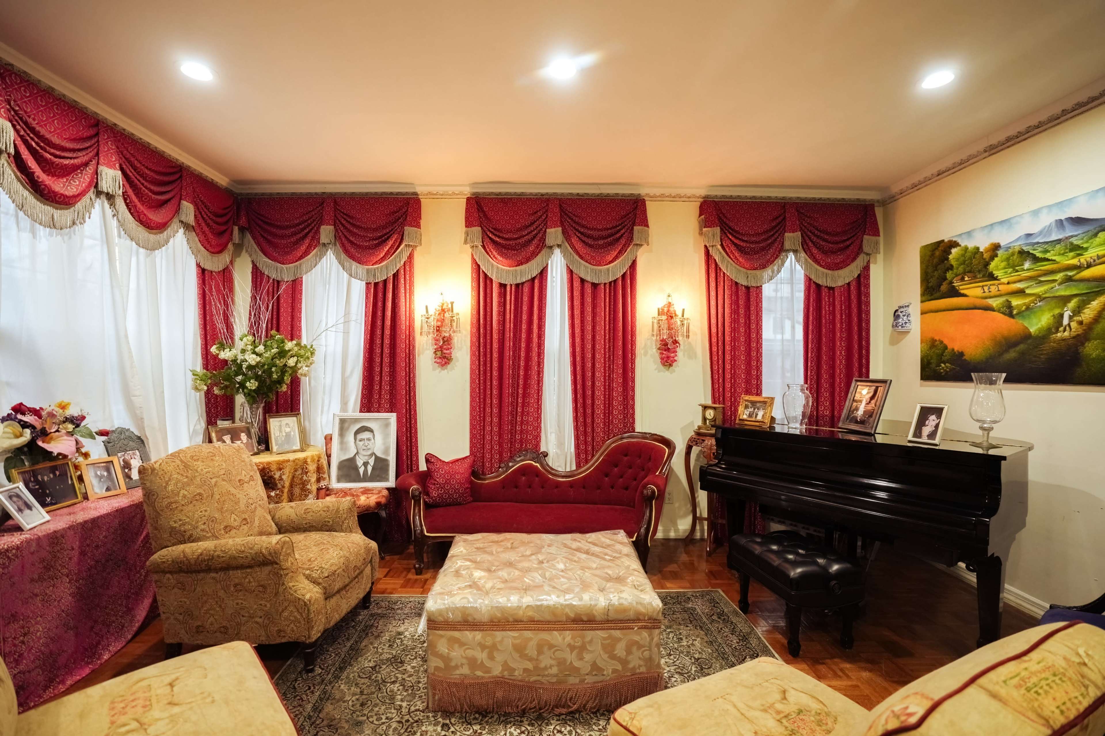The living room features elegant red drapes, a grand piano, a vintage sofa, and framed photographs on display.