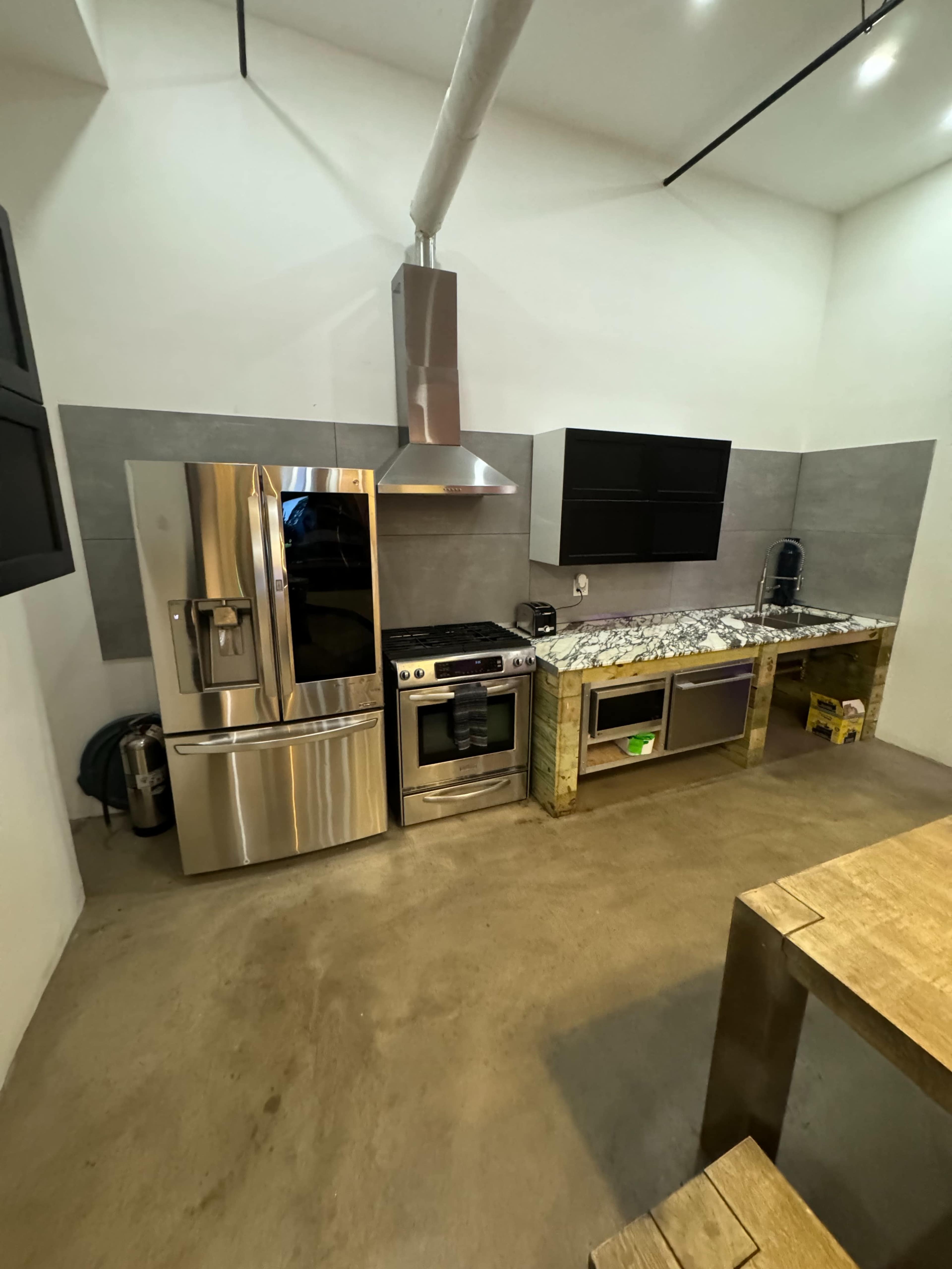 The image shows a modern kitchen with stainless steel appliances, including a refrigerator and oven, sleek cabinetry, and a concrete floor.