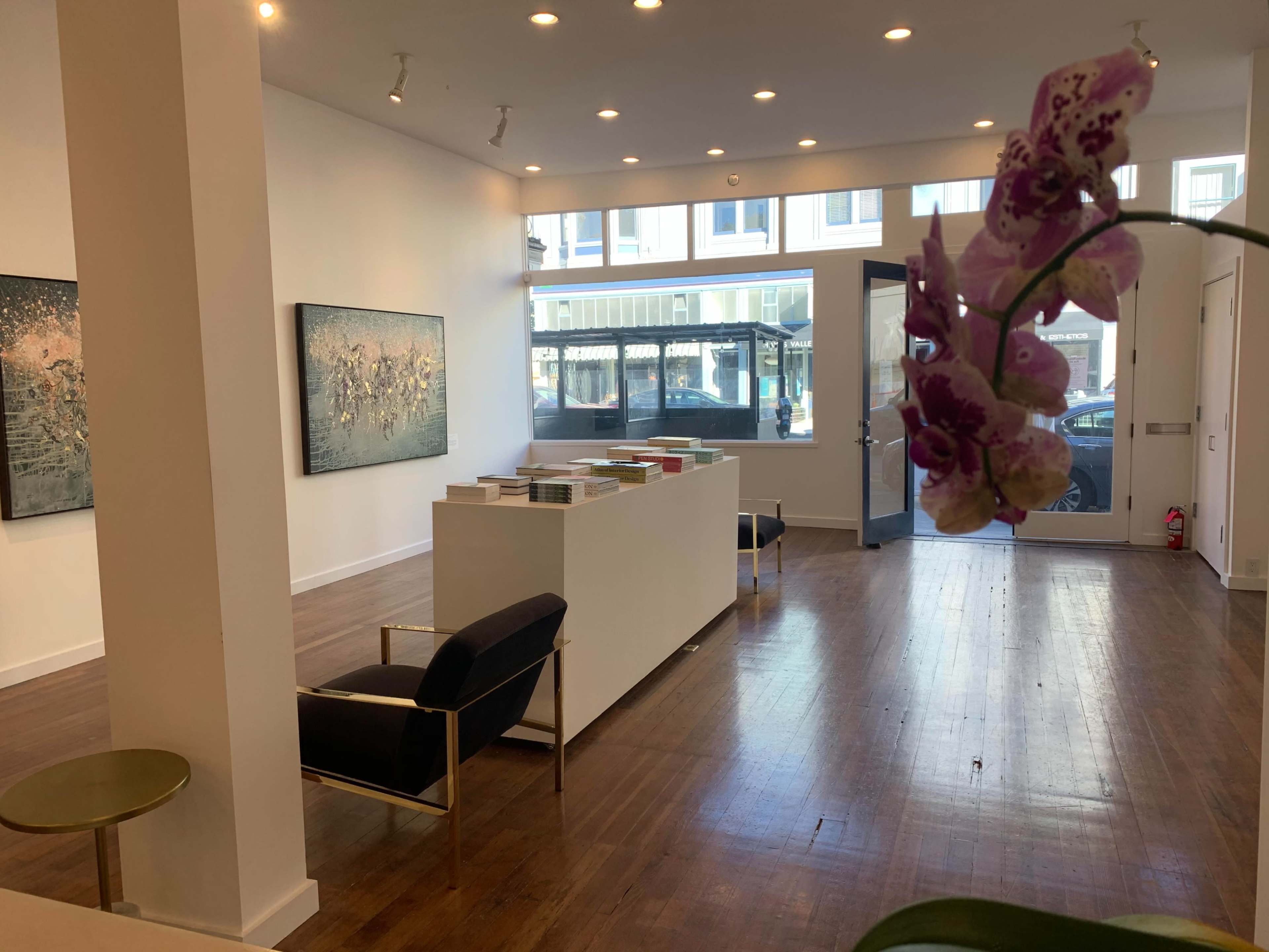 The image shows a spacious art gallery with two paintings on the wall and a central white display table surrounded by modern furniture.