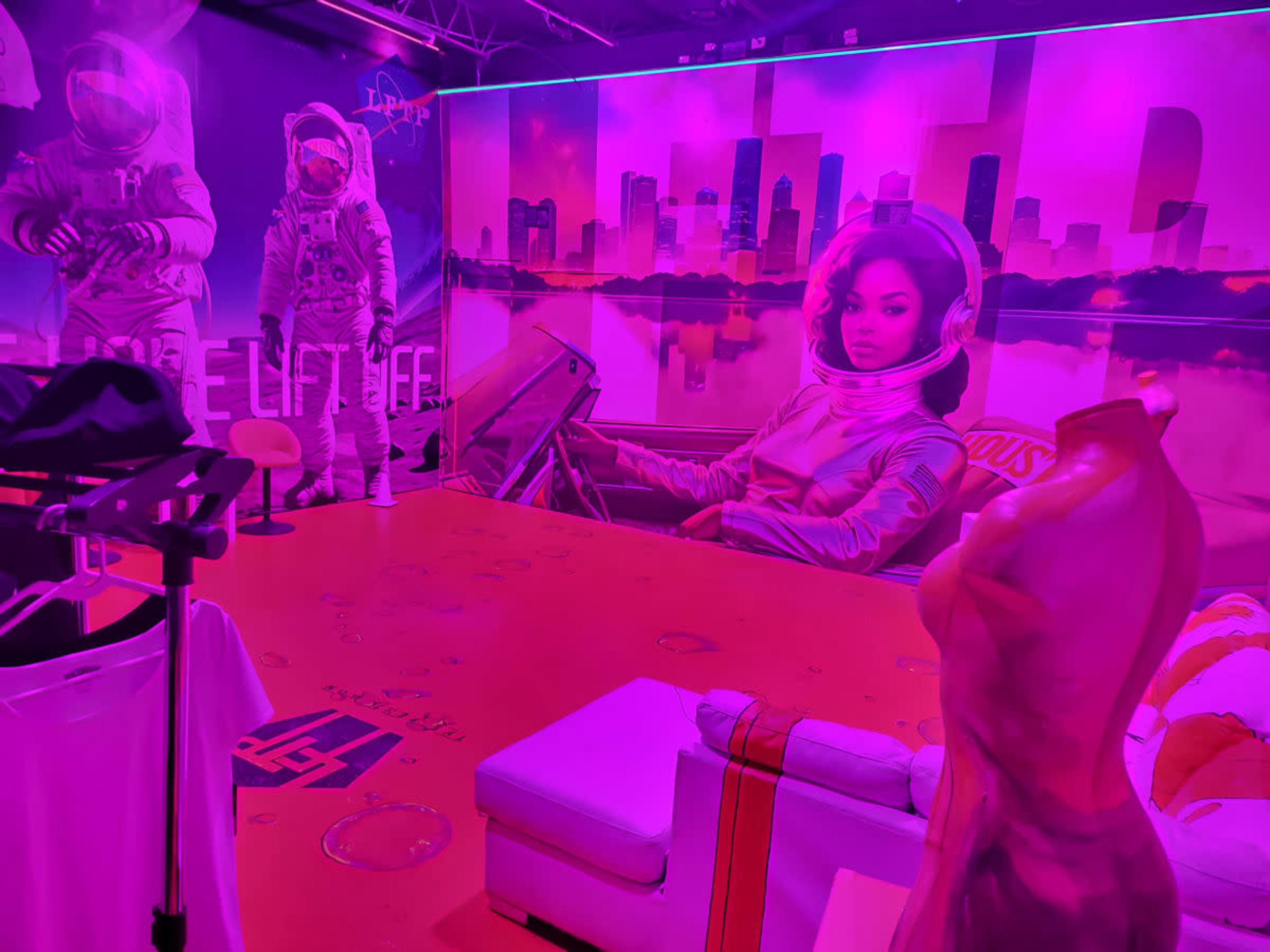 The room features vibrant pink walls adorned with large astronaut and space-themed murals, along with modern furniture and clothing on display.