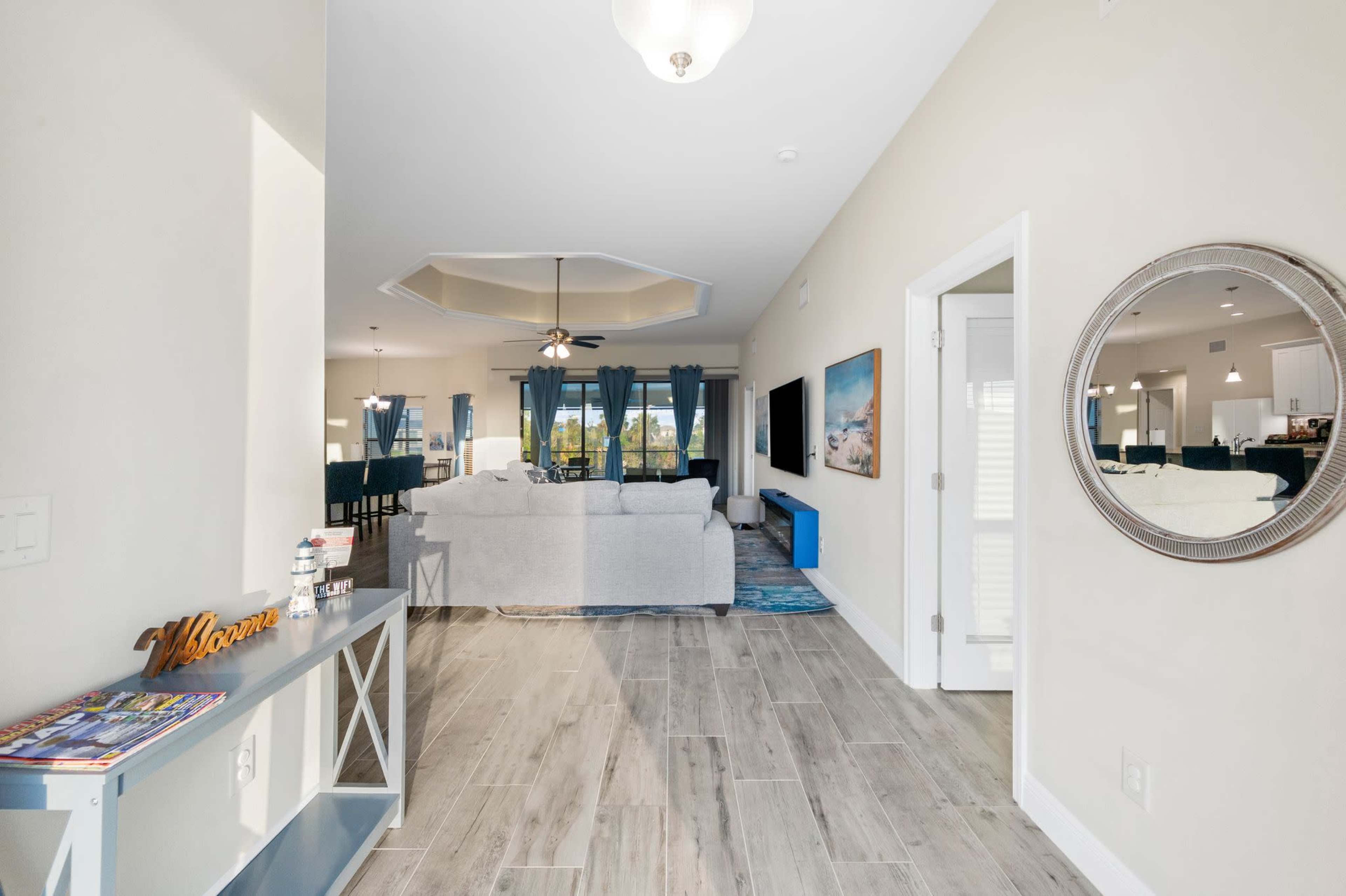The interior of a modern living space features a foyer with a console table, leading to a light-filled open living area furnished with a sofa and entertainment center.