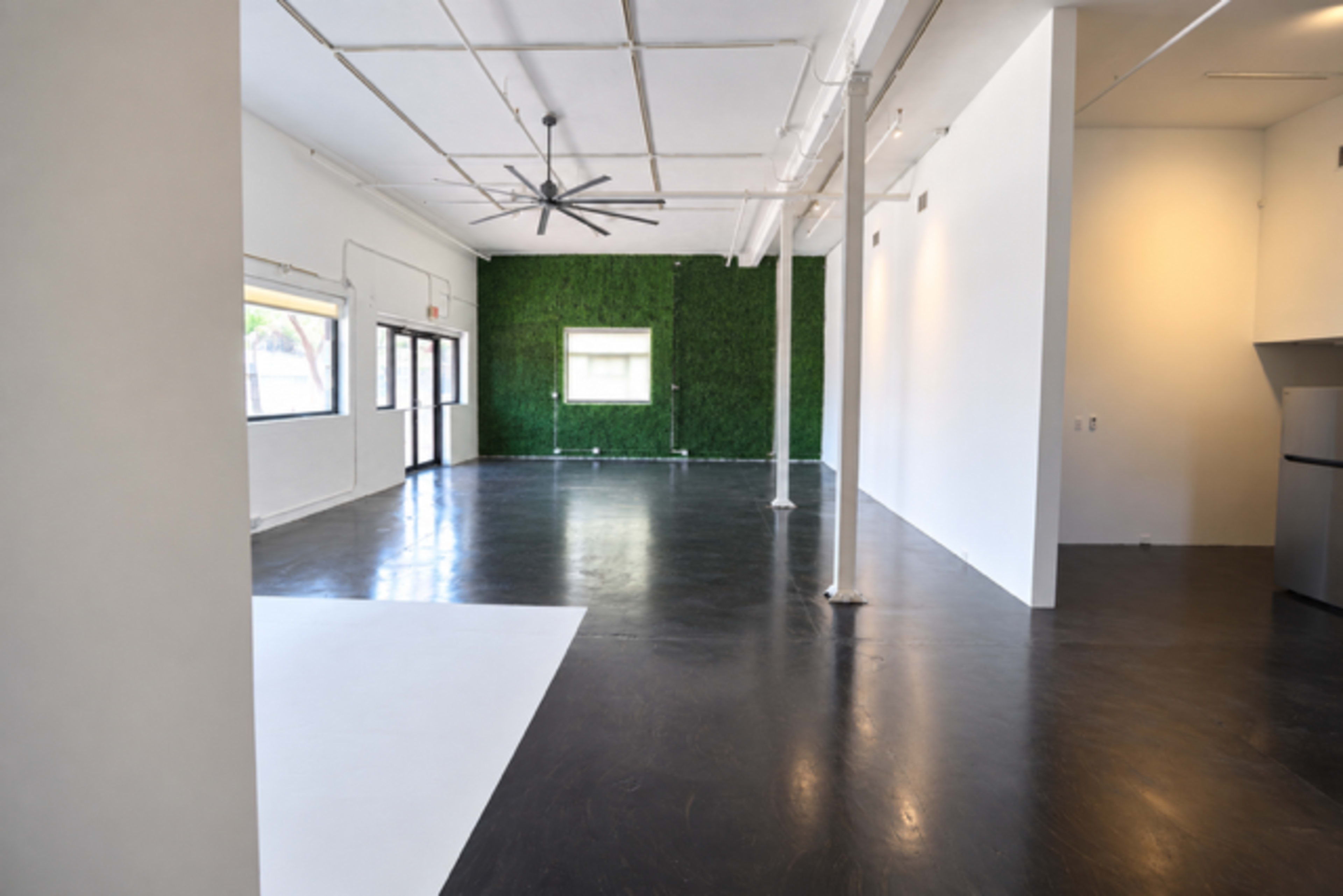 The image shows a spacious interior room with a polished dark floor, white walls, and a green accent wall made of artificial plants.